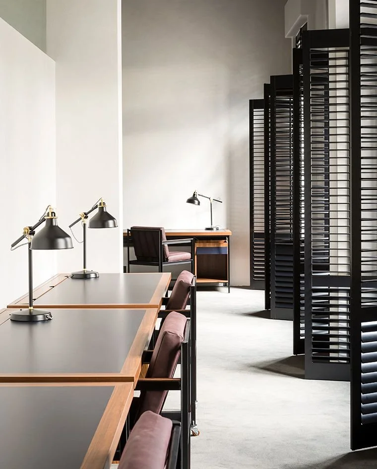 Een rustige, moderne studeerruimte met bureaus, tafelkampen, bureaulampen en louvredeuren of scheidingspanelen.