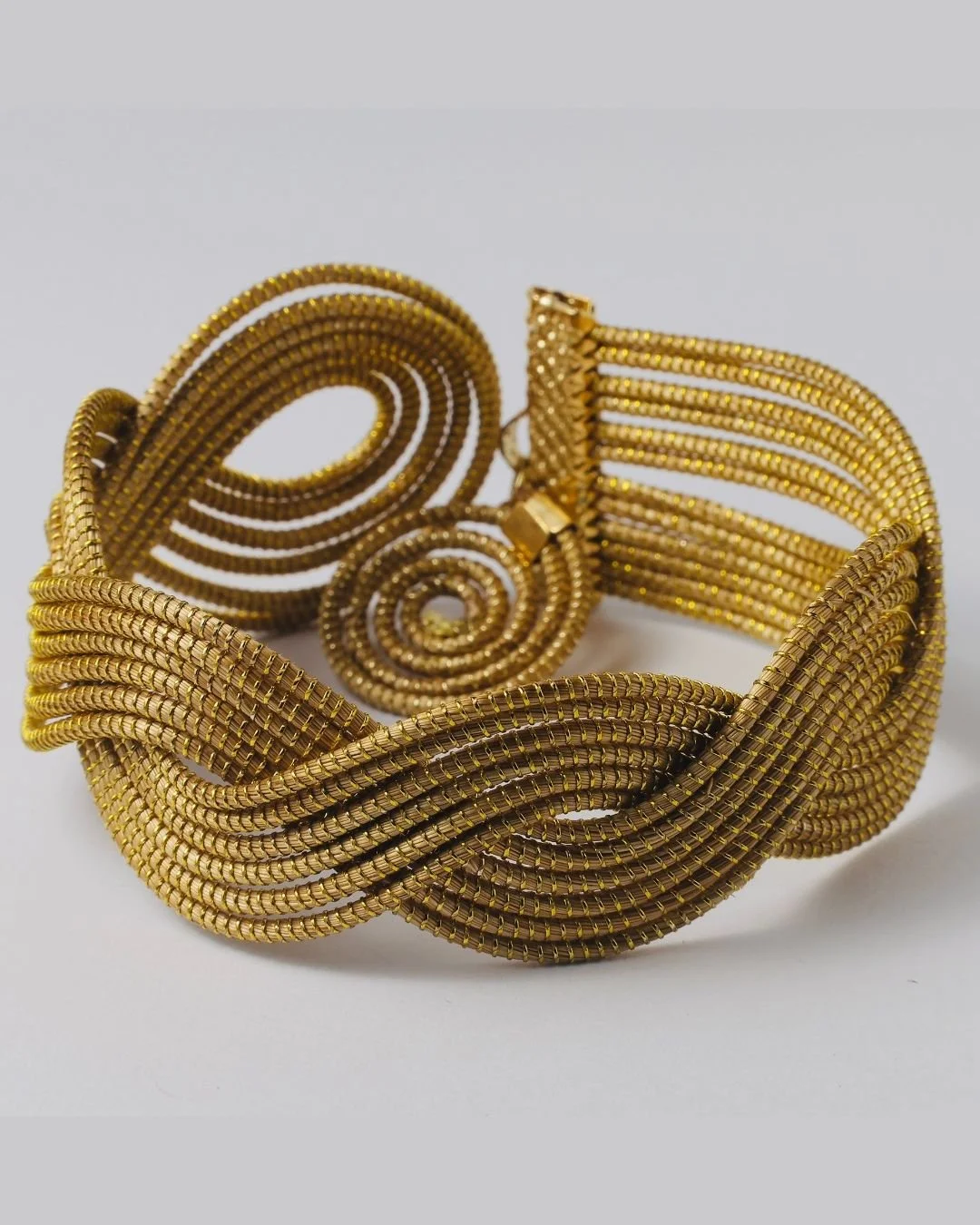 Ein goldener Schmuck mit verzierten spiralförmigen und gewundenen Designs, bestehend aus mehreren zusammengefügten Elementen.