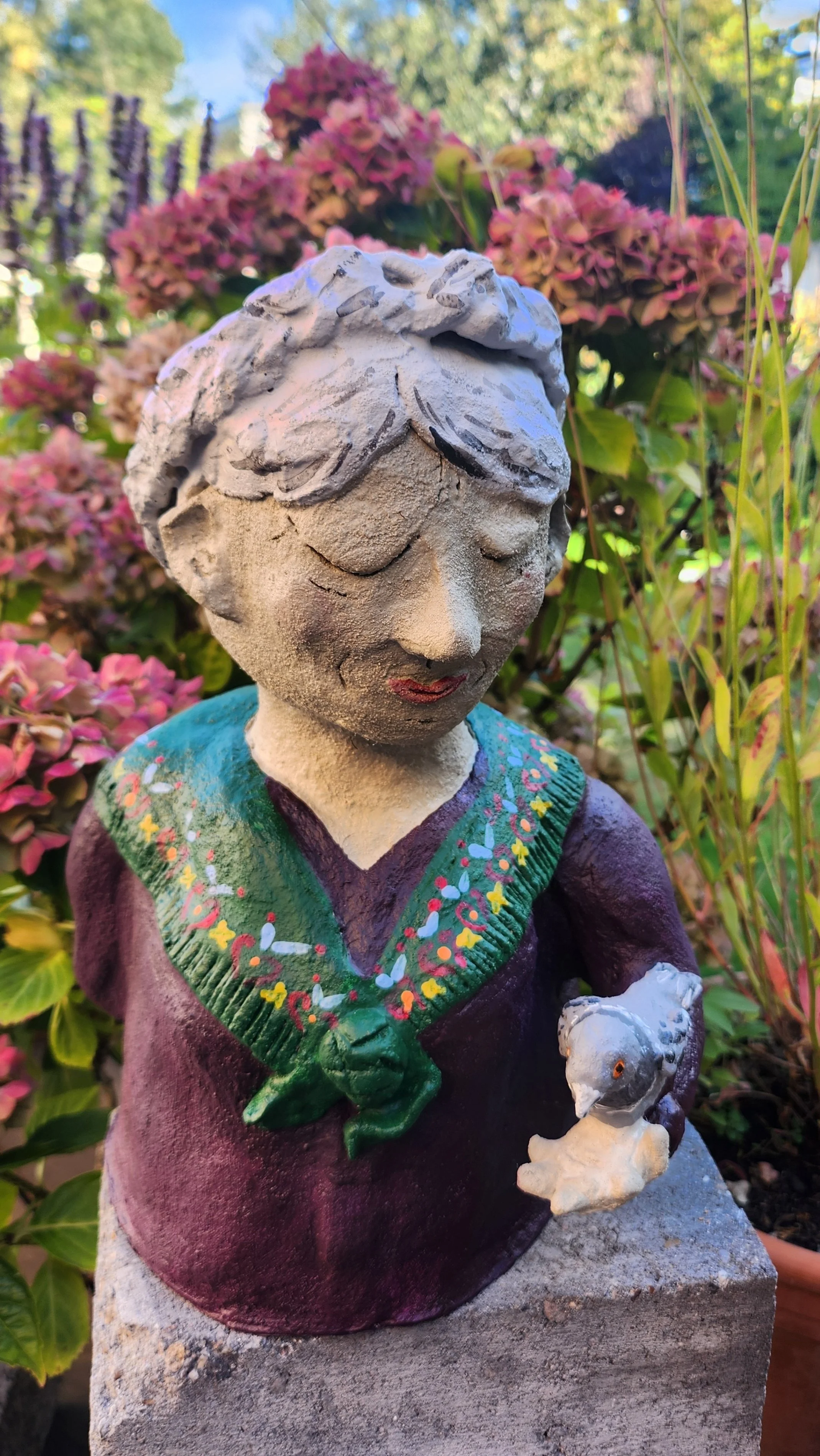 Gartenfigur eines Kindes mit einem kleinen Hund in der Hand, umgeben von bunten Blumen im Garten.