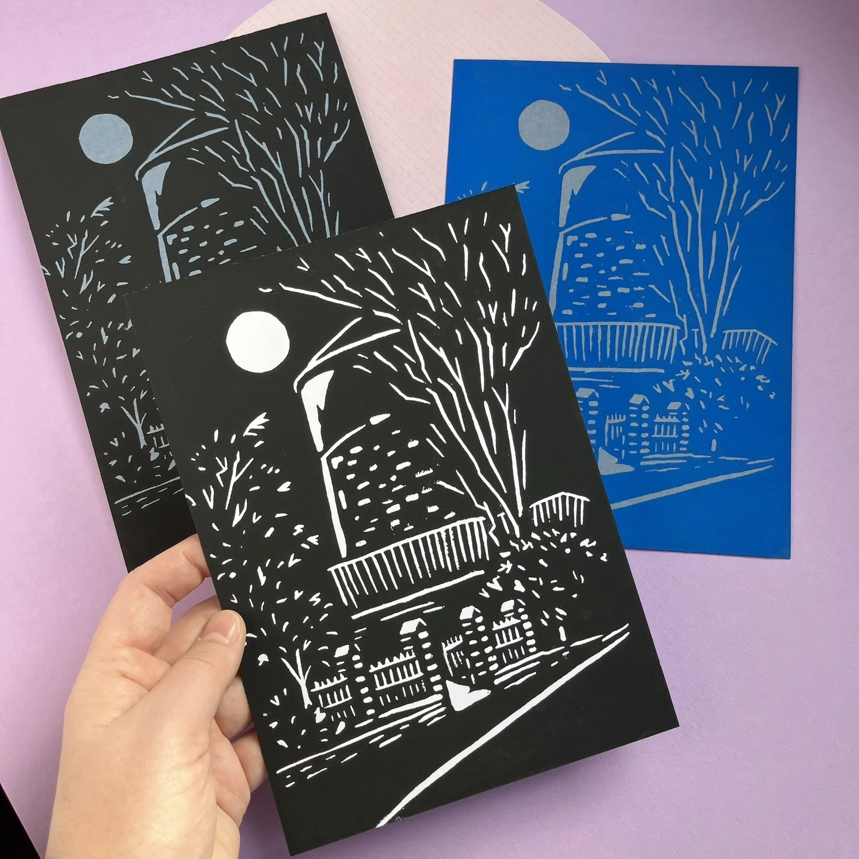 Papierkunstwerke in Silhouette von Stadt und Natur bei Nacht, mit Mond am Himmel, festem Zaun und Bäumen.