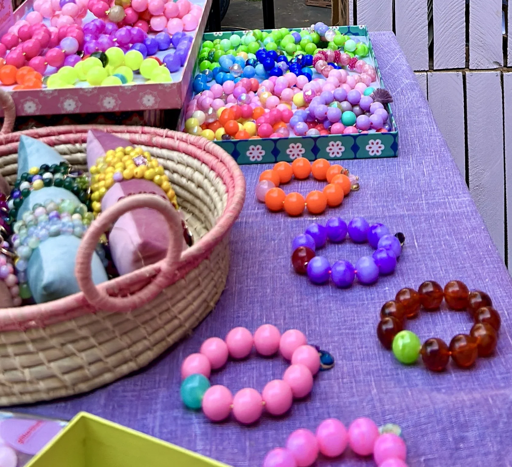 Bunte Armbänder und bunte kleine Gummibälle auf einem Tisch mit lila Tischdecke.