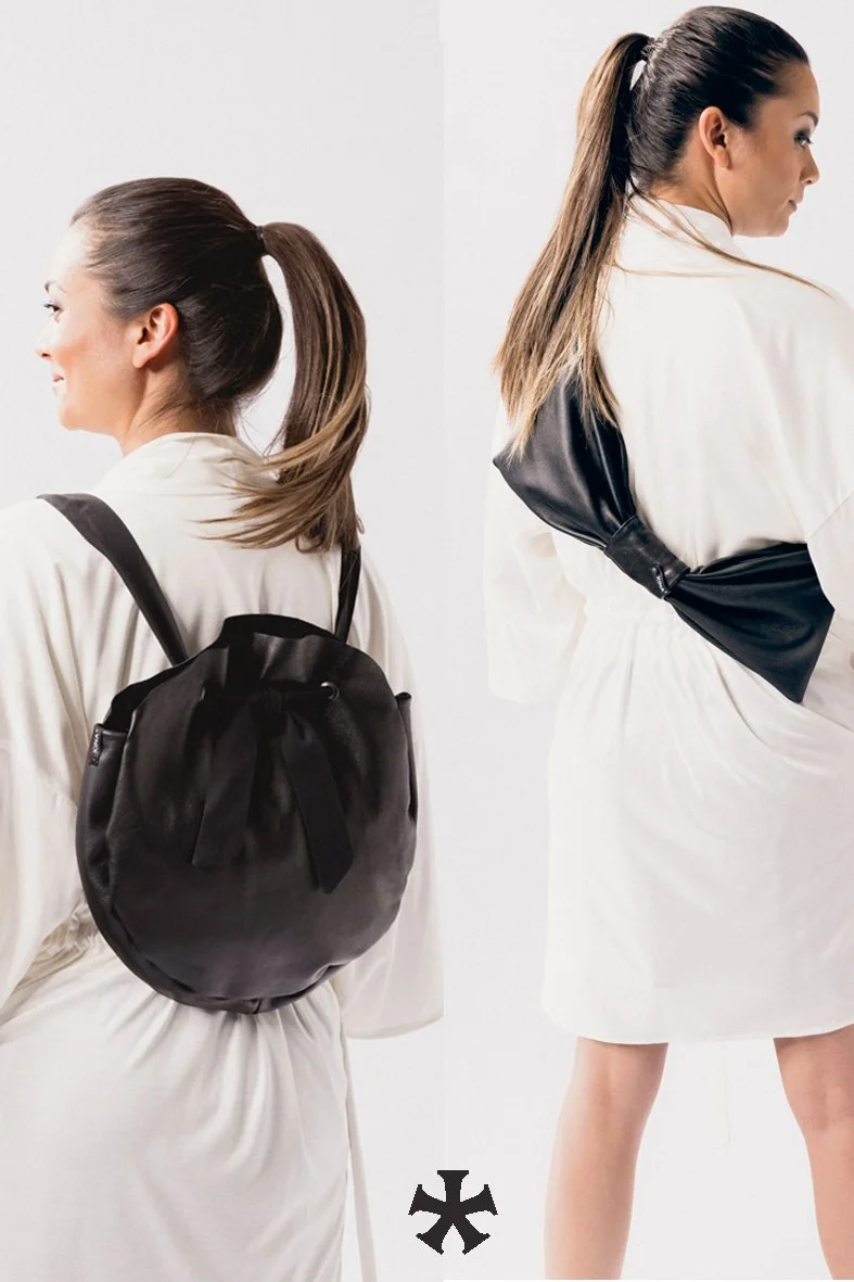 Zwei Frauen, die Rückenansichten zeigen, tragen weiße Kleidung und tragen schwarze Taschen. Die Frau links hat einen Rucksack, die Frau rechts eine Umhängetasche.