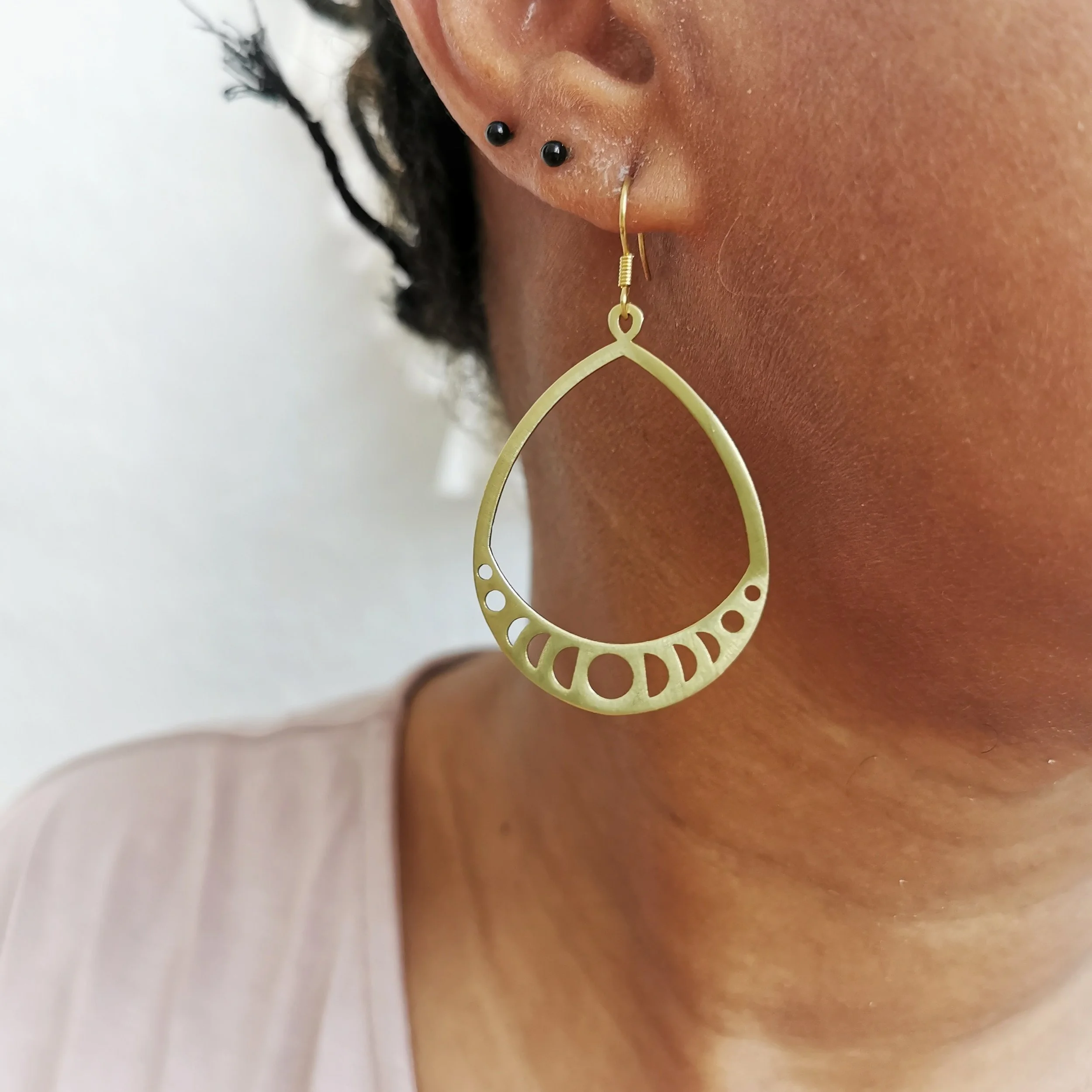 Nahaufnahme eines Ohrläppchens mit mehreren Piercings, tragend eine große, goldene Ohrring in der Form einer Tropfen-Öse mit kreisförmigen Aussparungen