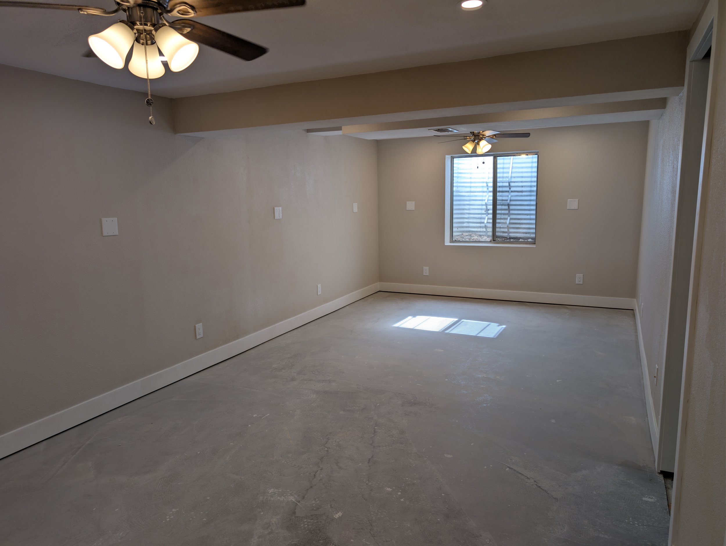 Empty room with beige walls, a window with metal security bars, a ceiling fan with lights, and a light-colored carpet.