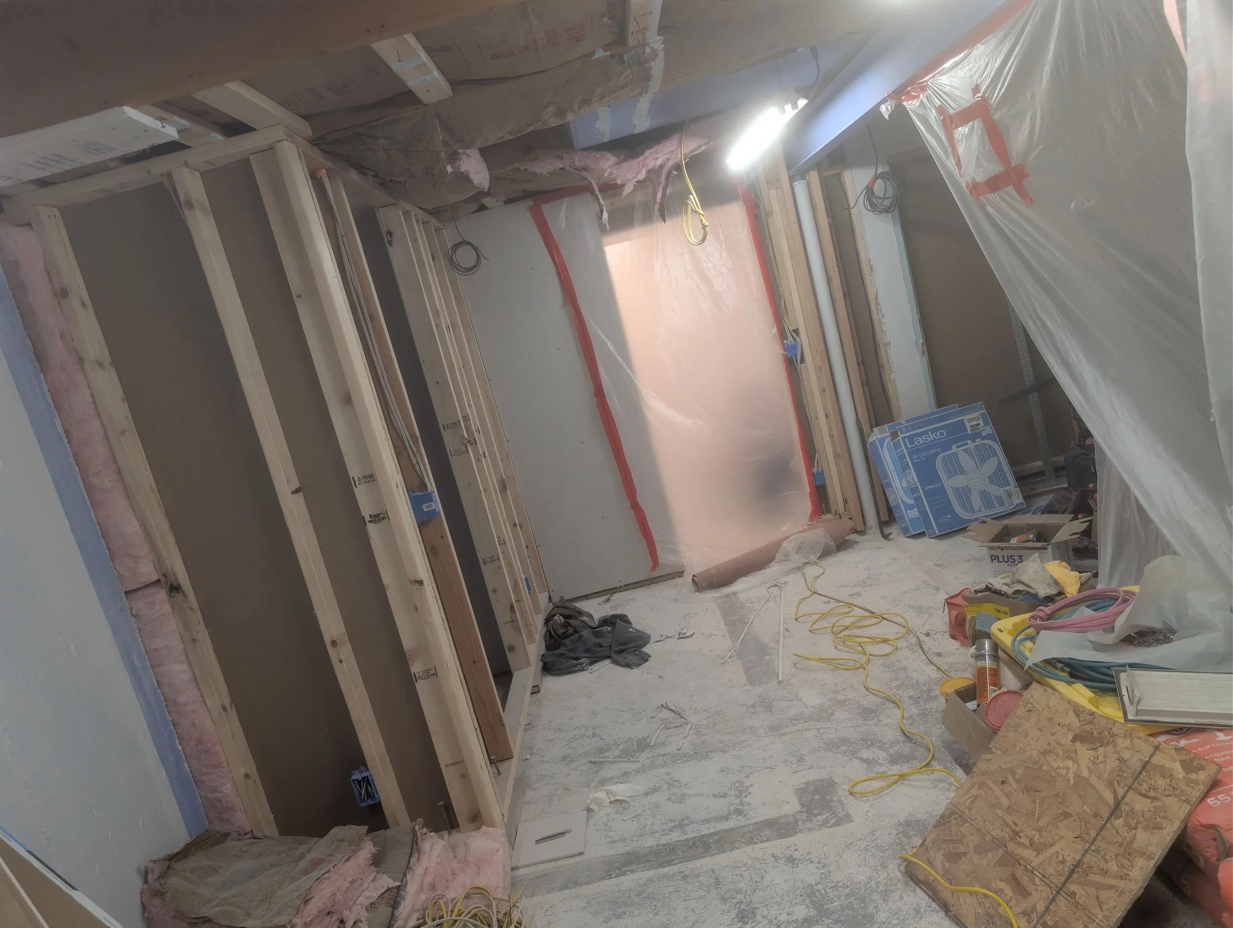 Construction site inside a building with framing, insulation, electrical wiring, and plastic sheeting covering areas for drywall installation.