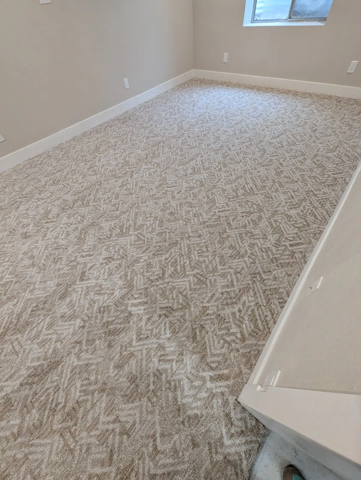 Empty room with beige patterned carpet, white walls, and a window on the ceiling letting in natural light.