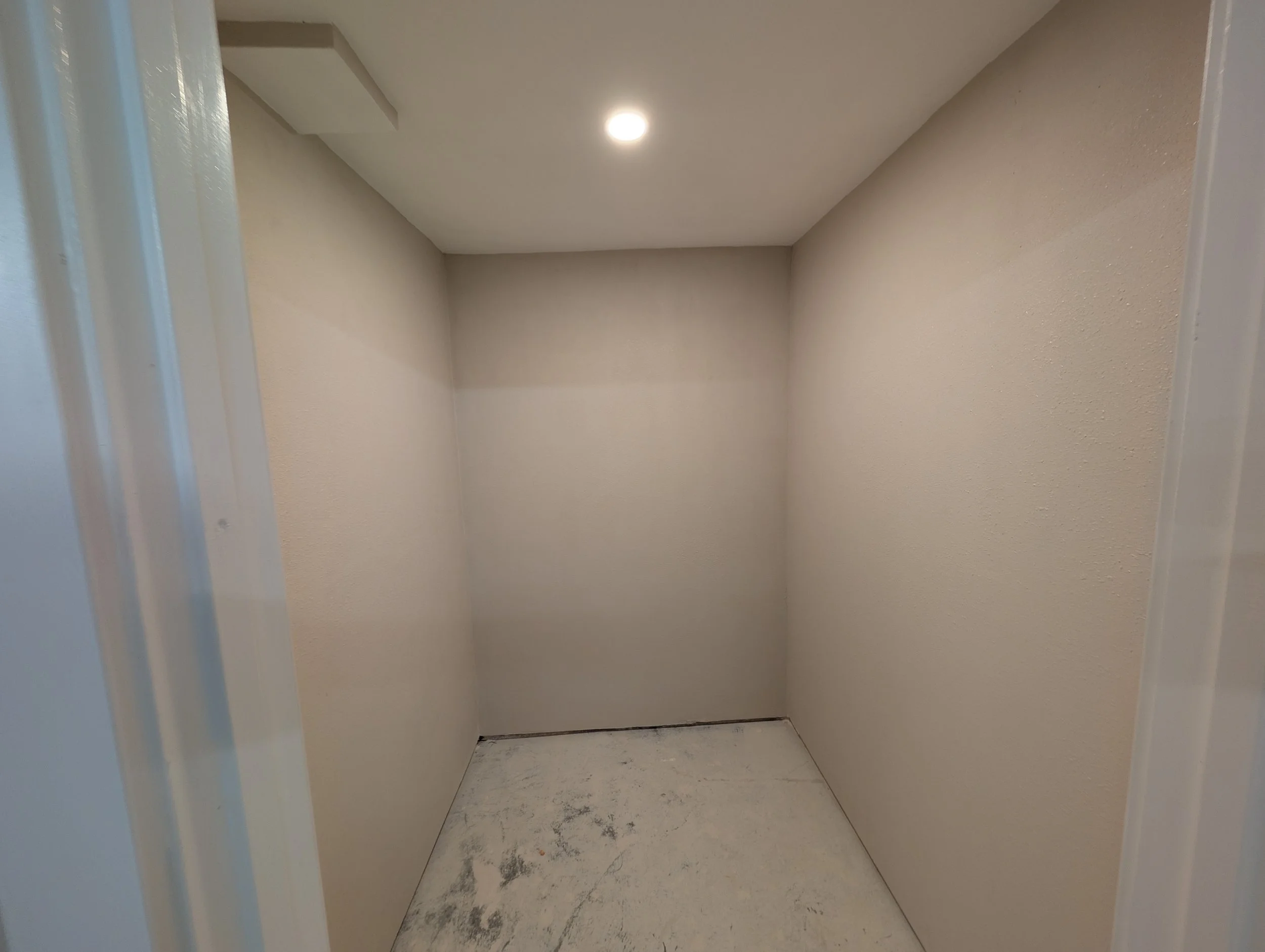 Empty elevator with beige walls and a white ceiling, featuring a single ceiling light and a dirty floor with black marks.