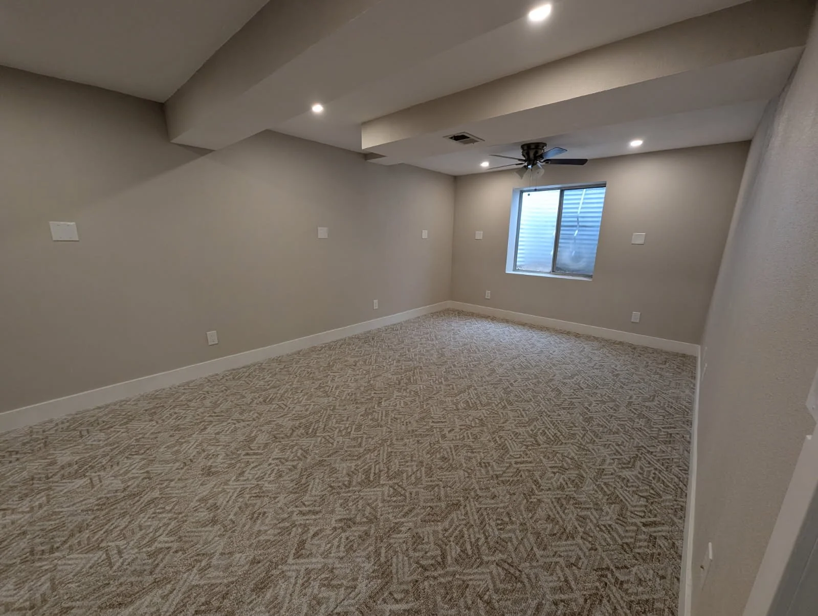 Empty room with beige walls, a patterned carpet, a window with blinds, and a ceiling fan. Recessed lighting is installed in the ceiling.