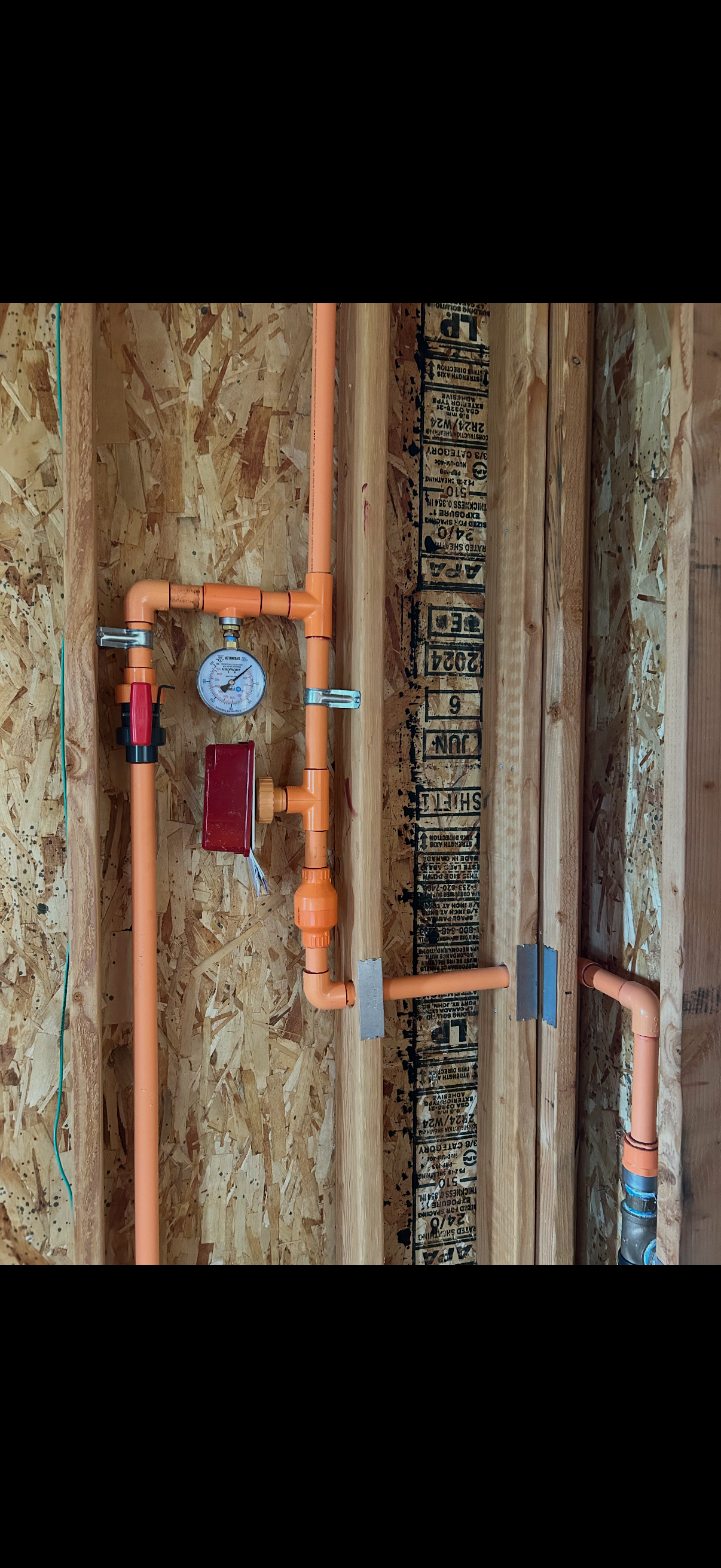 Residential fire sprinkler inspection assembly with pressure gauge and control valve installed inside wall framing during construction.