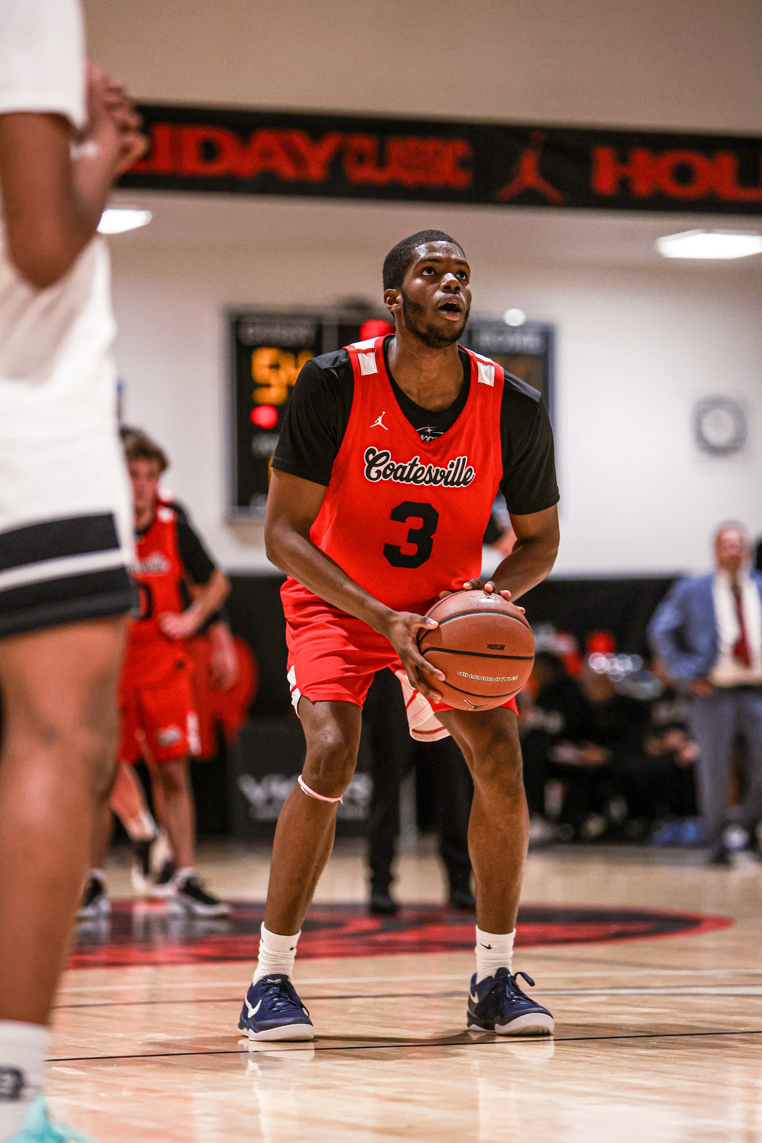 Two high school basketball players competing for possession of the ball on the court, with banners hanging in the background.