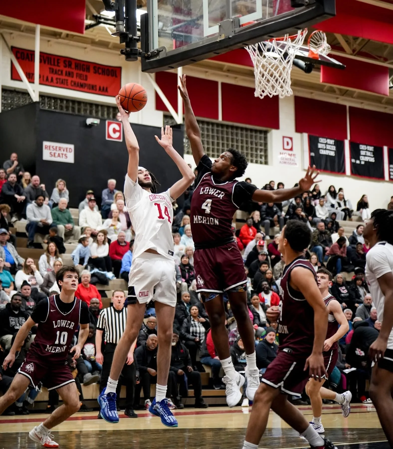 Two high school basketball players competing for a rebound near the basket, with a crowd of spectators in the background.
