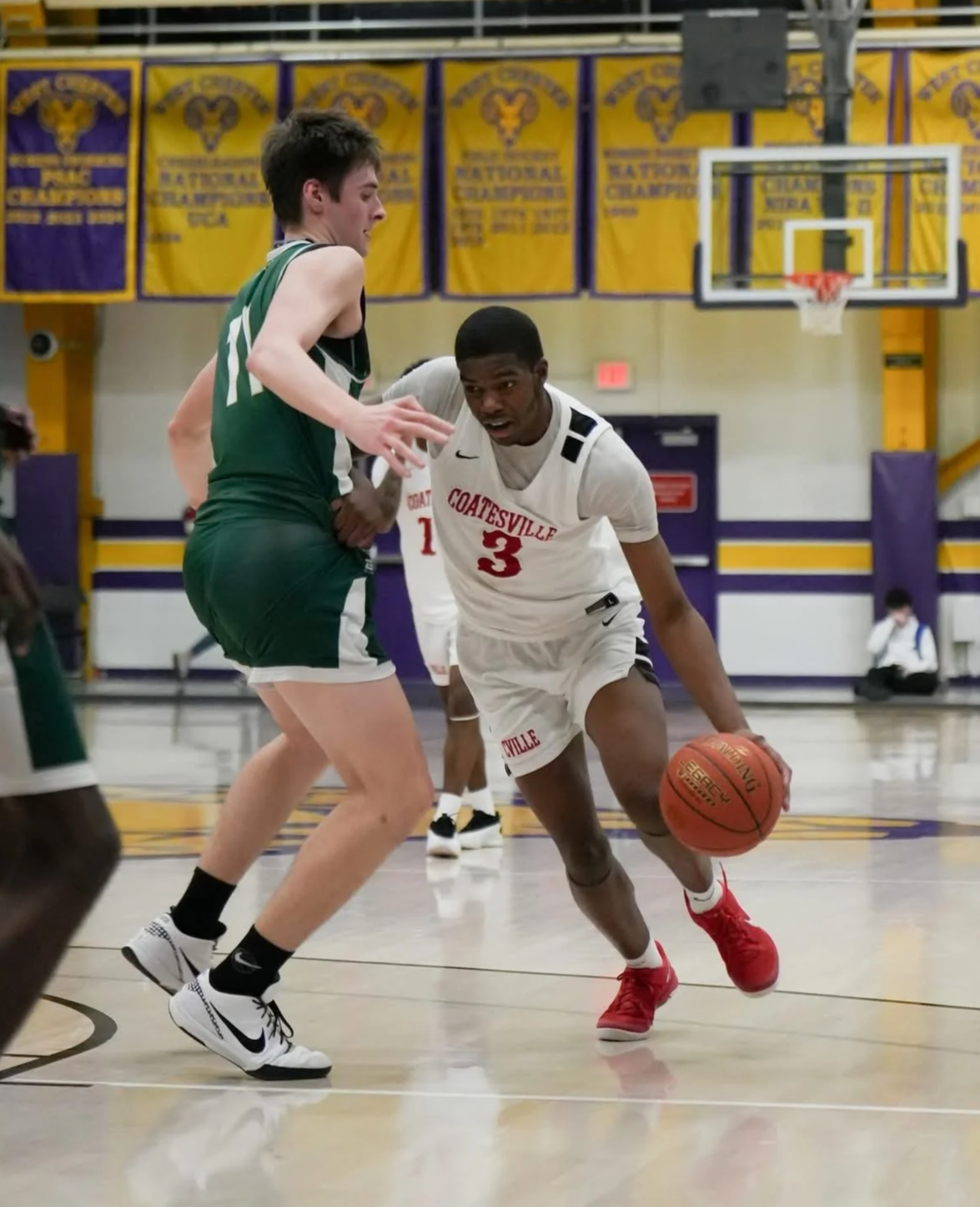 Two high school basketball players competing for possession of the ball on the court, with banners hanging in the background.