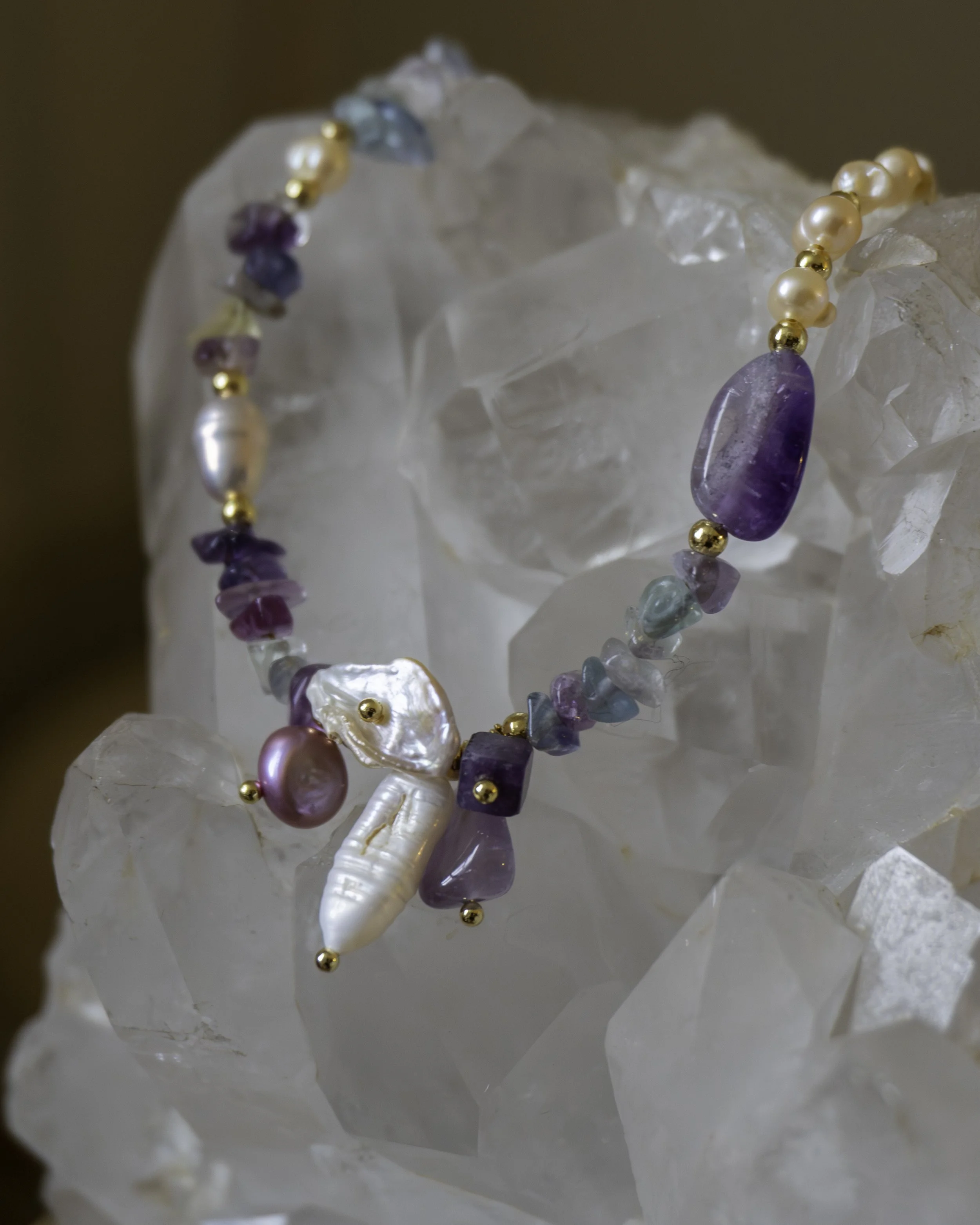 A necklace with purple, pearl, and turquoise beads resting on a translucent crystalline rock.