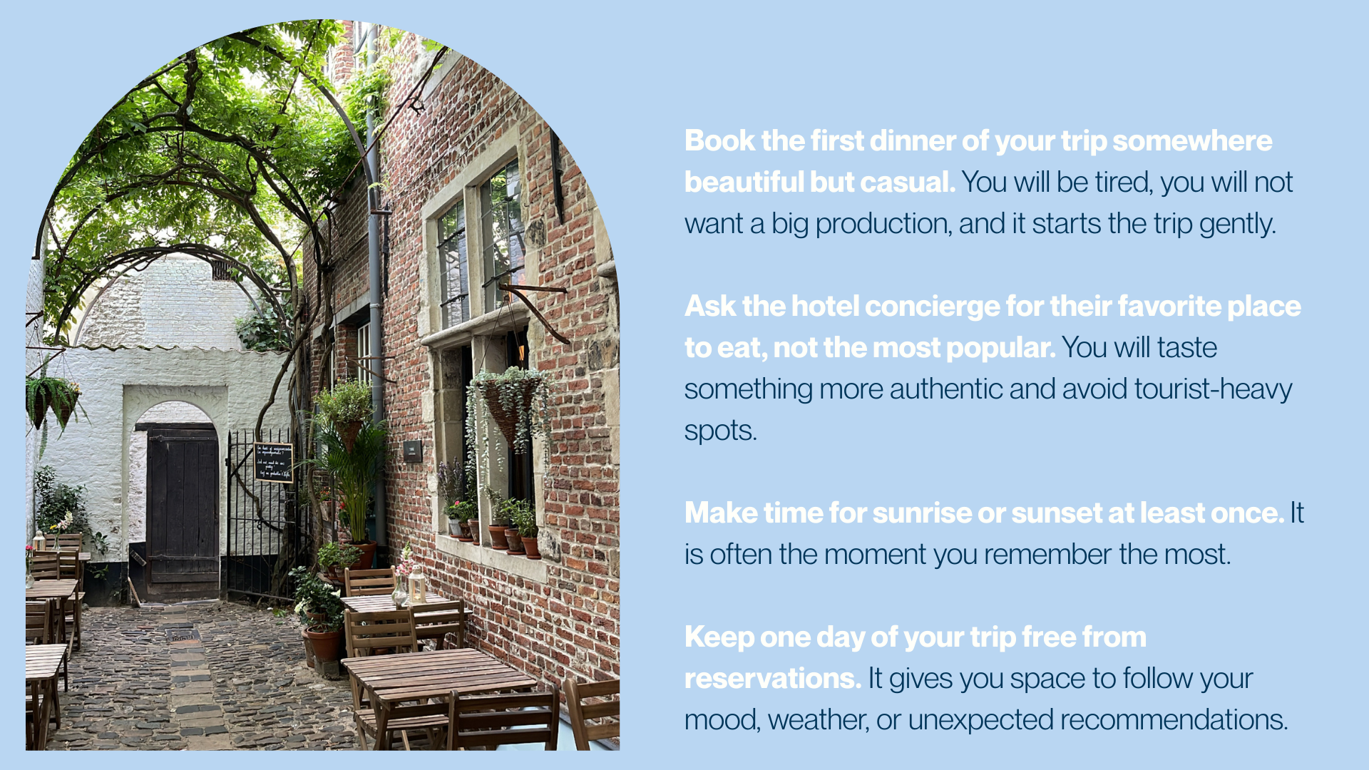 A cozy outdoor patio with cobblestone paving, surrounded by brick and whitewashed walls, potted plants, wooden tables and chairs, and a decorative arched tree above.