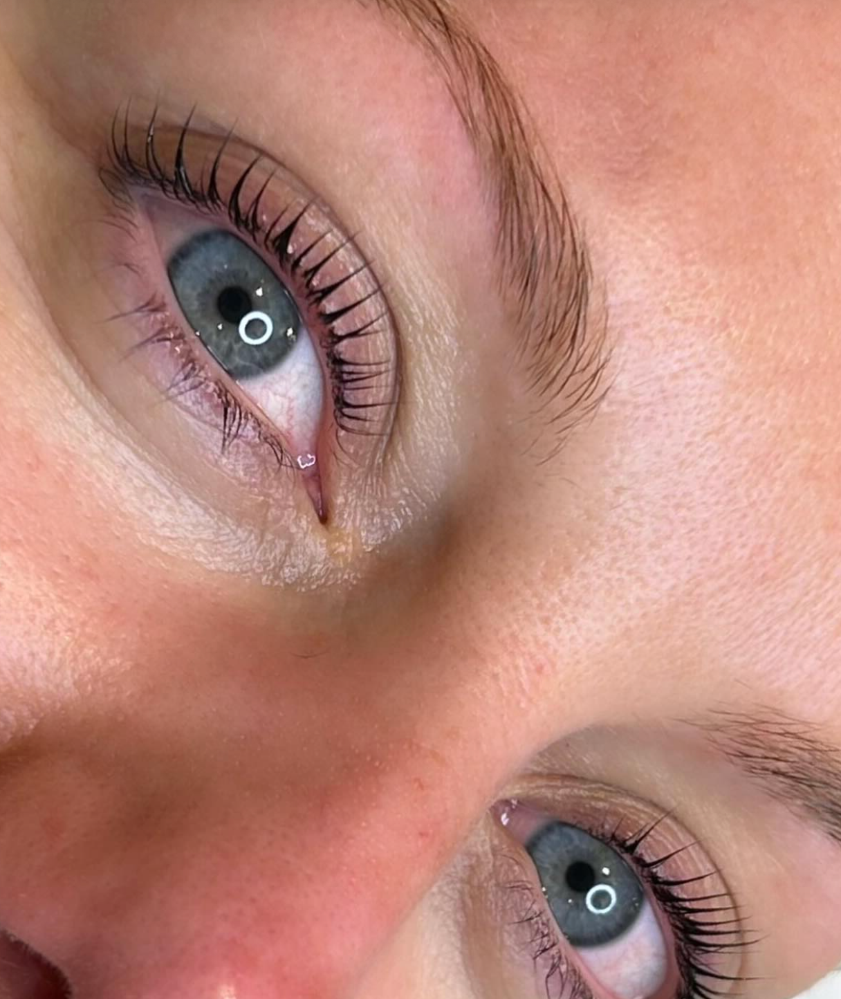 Close-up of a person's face focusing on the eyes, showing blue irises, long eyelashes, and light skin with visible pores.