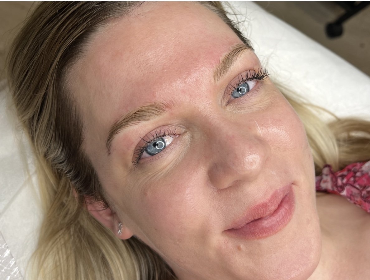Close-up of a woman's face with clear skin, blue eyes, and blonde hair, lying down on a white surface.