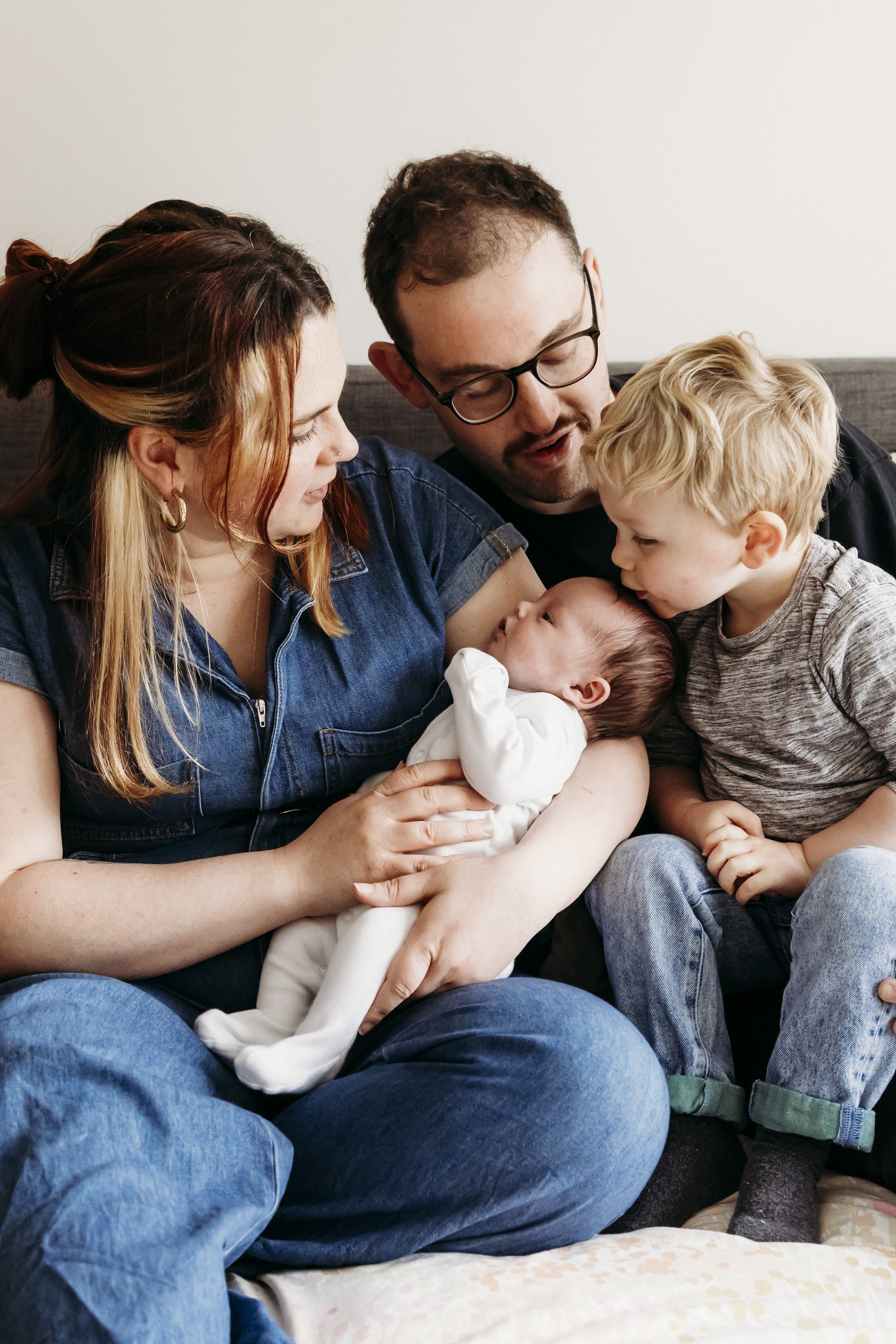 A family with two adults and two children gathered around a newborn baby, all sitting on a couch in a living room.