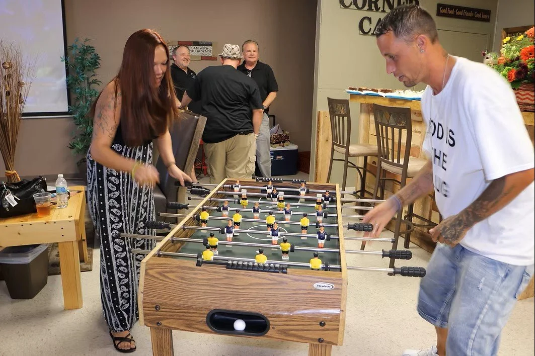 Two people playing foosball in a room with several onlookers in the background.