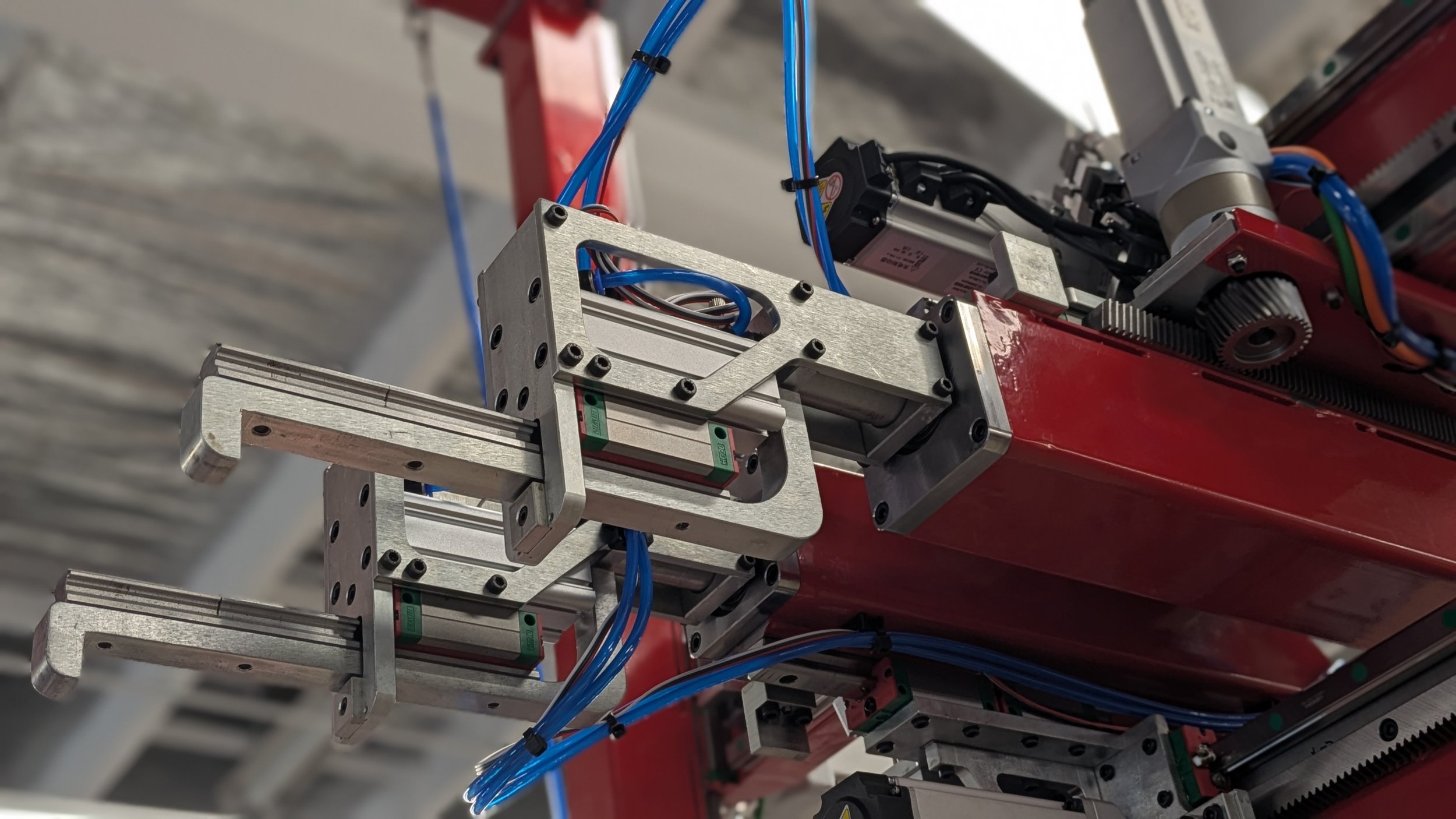 Close-up of a mechanical robotic arm with metal components, blue wires, and gears in an industrial setting.