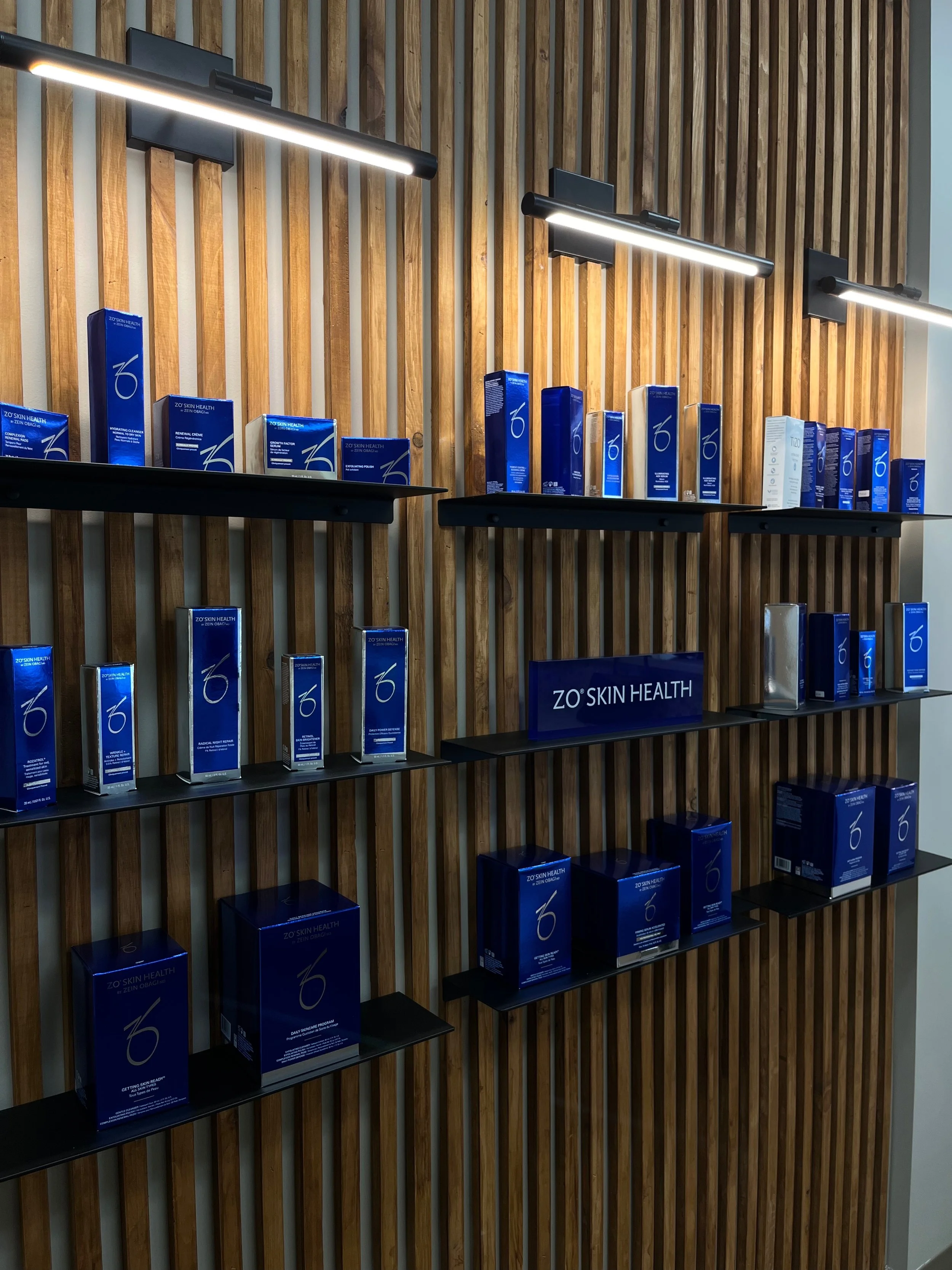 Display of ZO'Skin Health products on black shelves against a wooden slat wall under modern lighting.