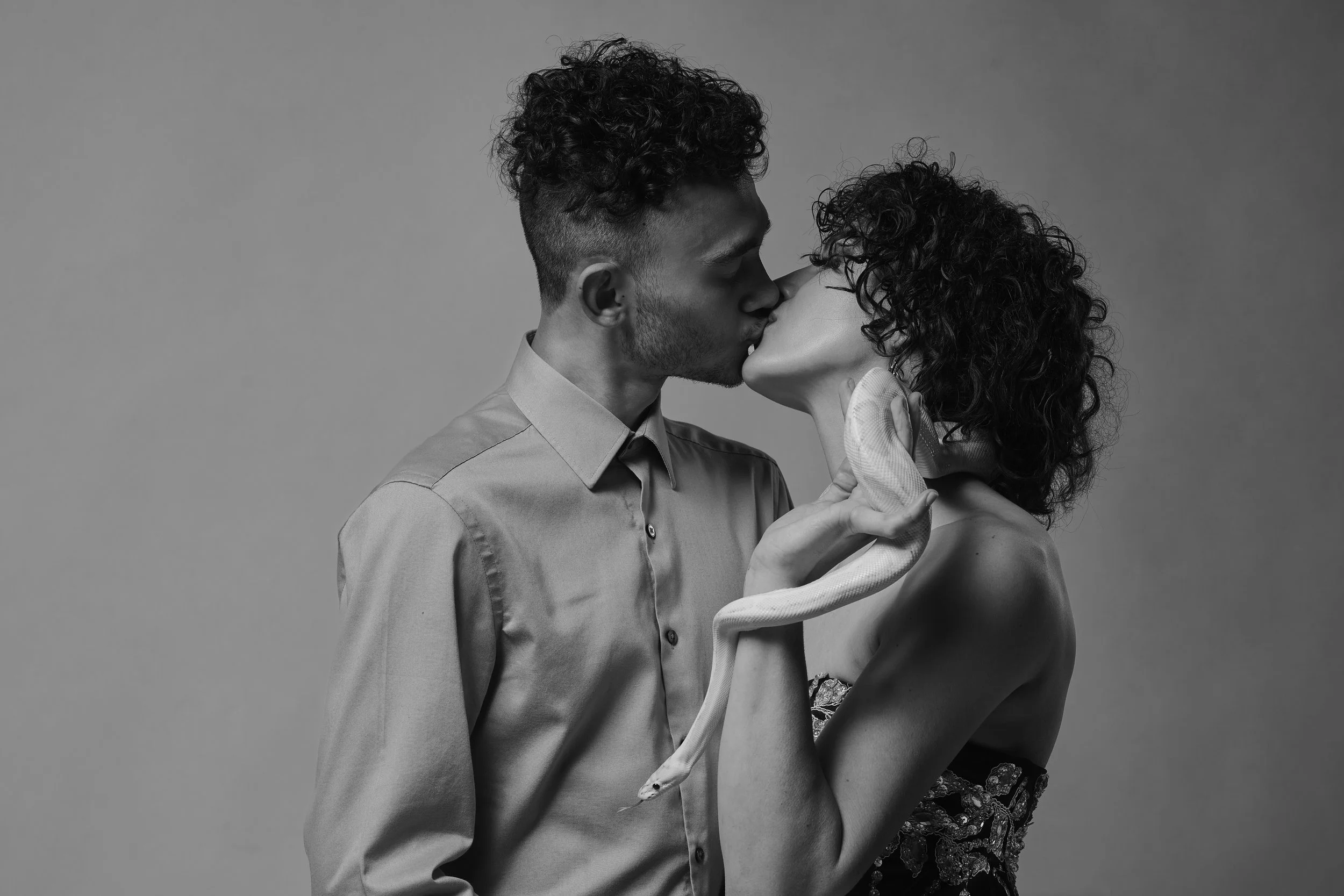 A black and white photo of a couple kissing, with a snake wrapped around the woman's arm.