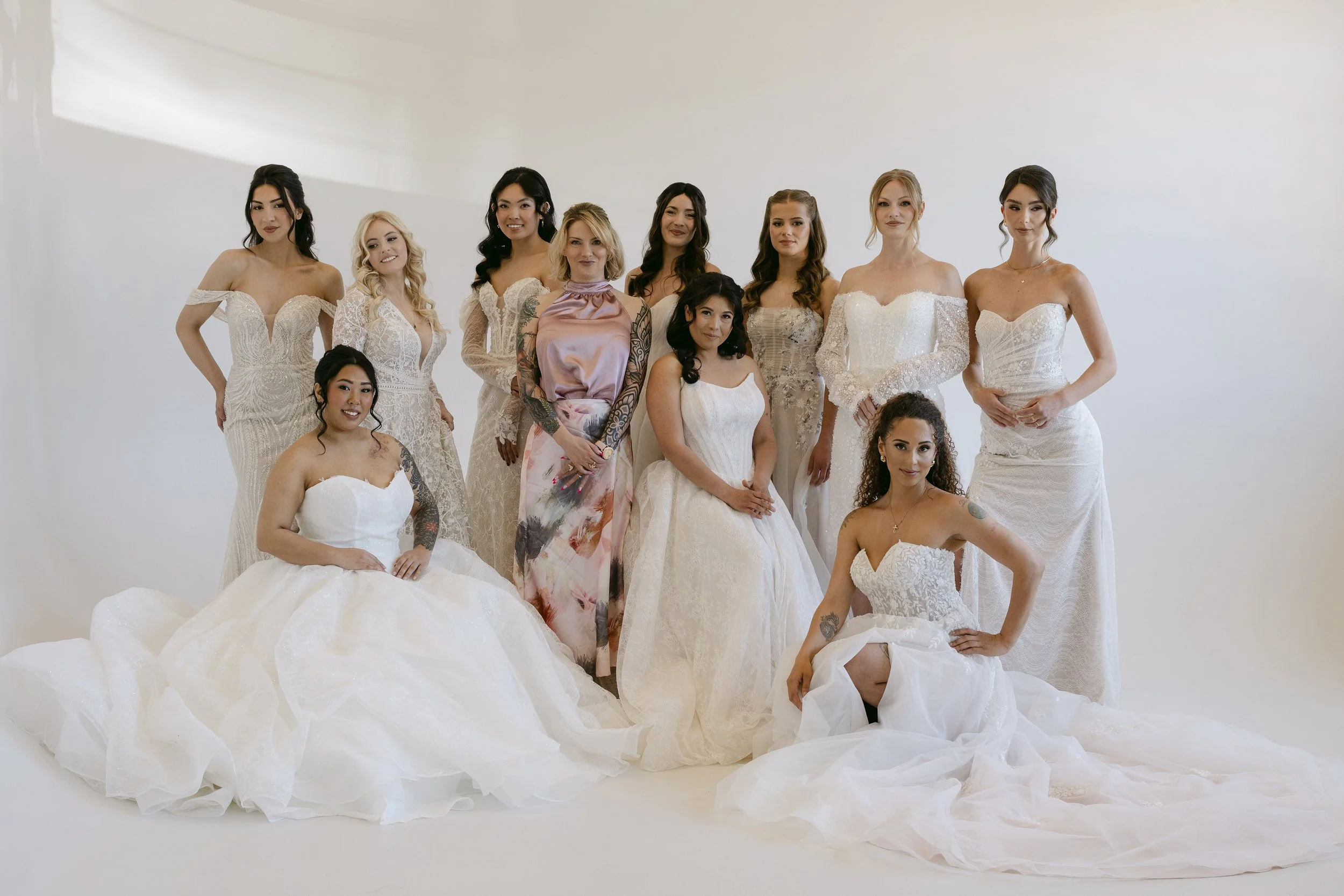 A photo of Kate, owner of Lucky Charm Bridal, with brides wearing a variety of wedding dresses from her bridal shop