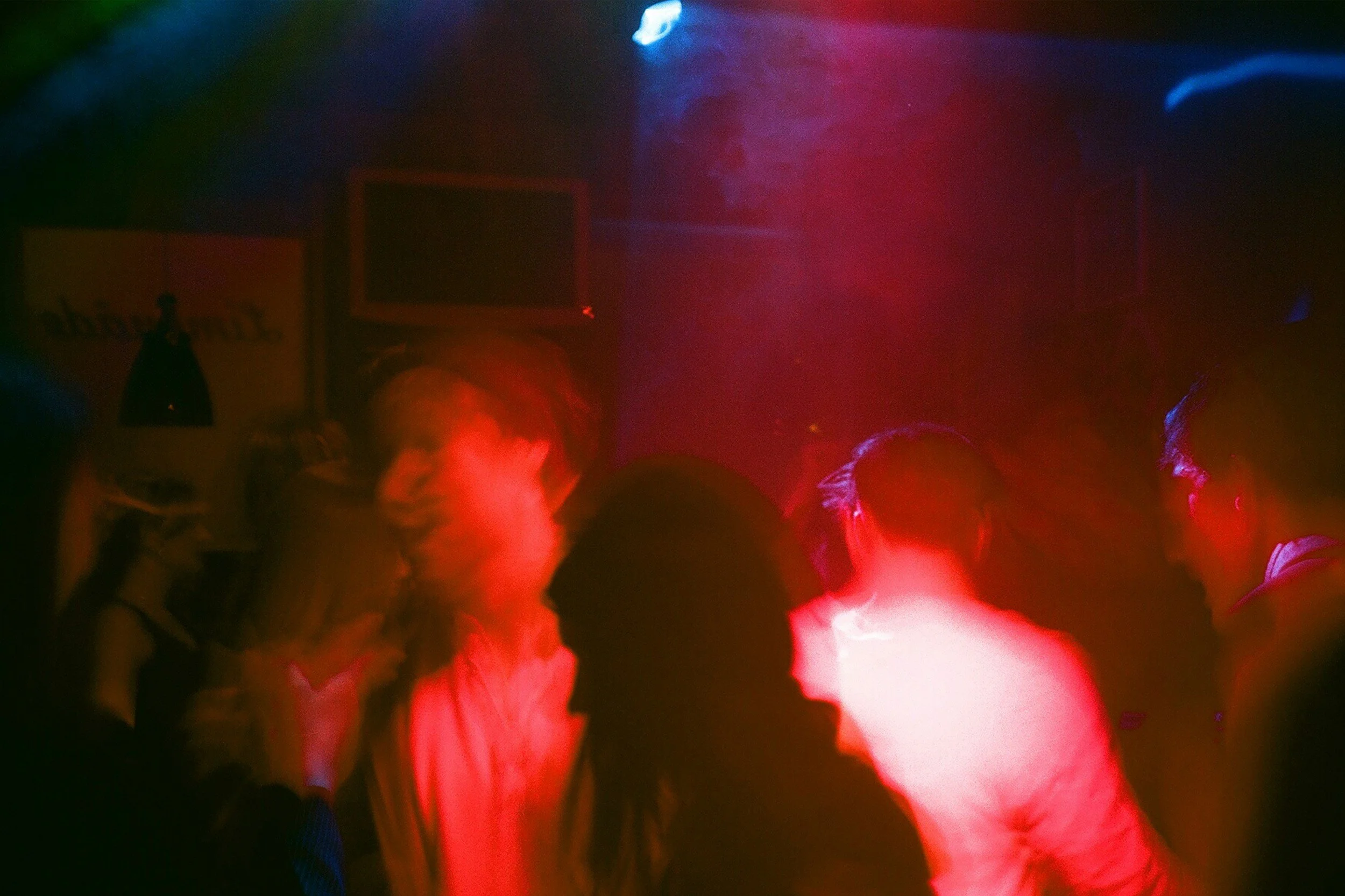 People dancing in a dimly lit nightclub with pink and blue lighting.