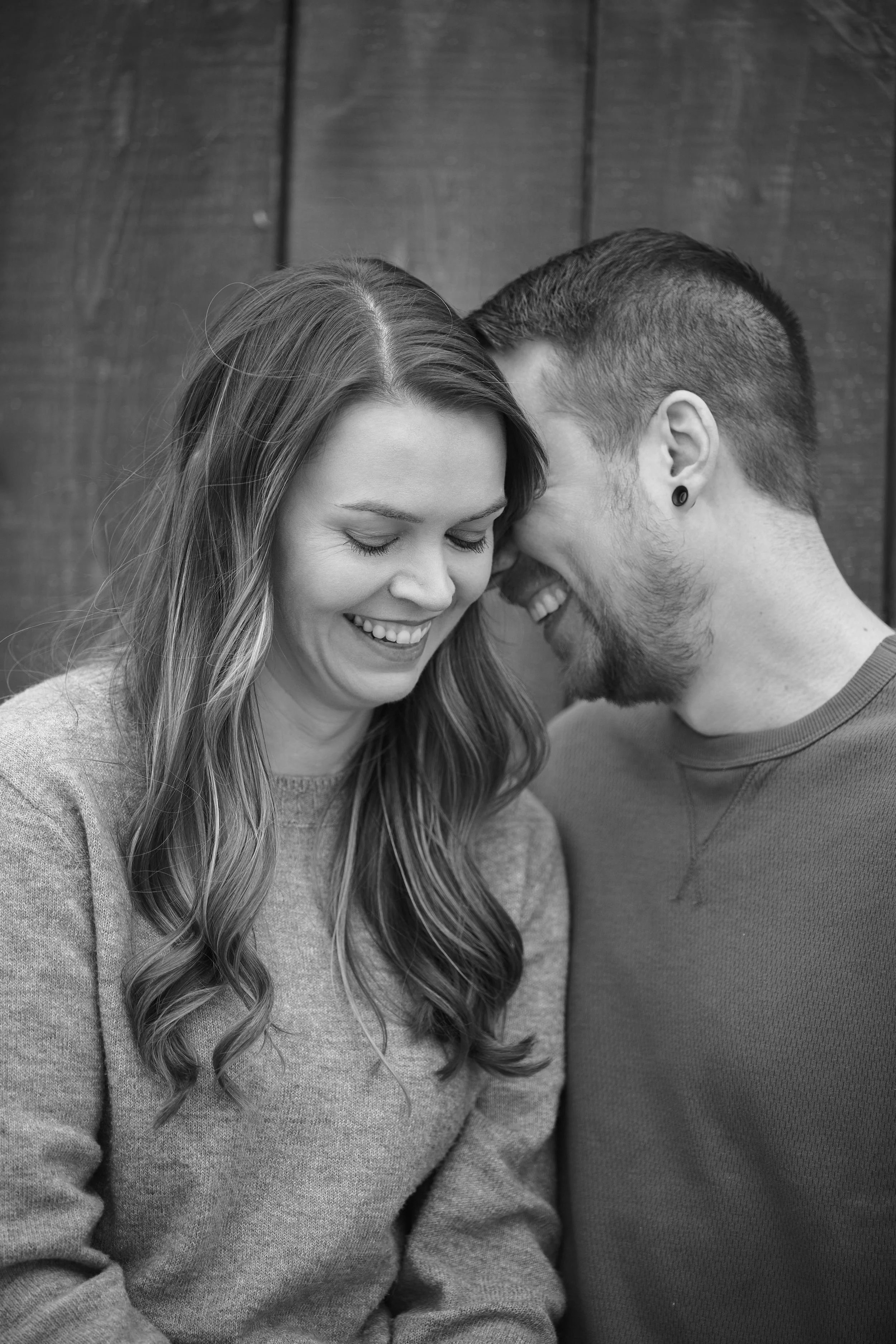 A black and white photo of a smiling woman and man leaning their foreheads together, appearing happy and affectionate.