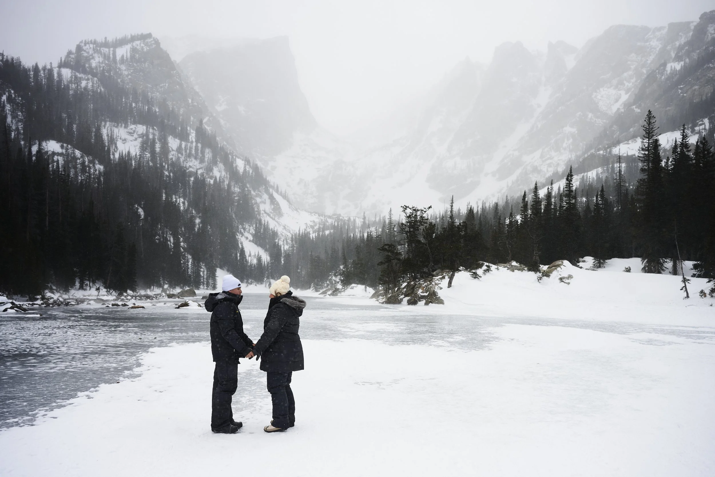 A couple hold hands standing on the ice of a frozen lake in Rocky Mountain National Park.