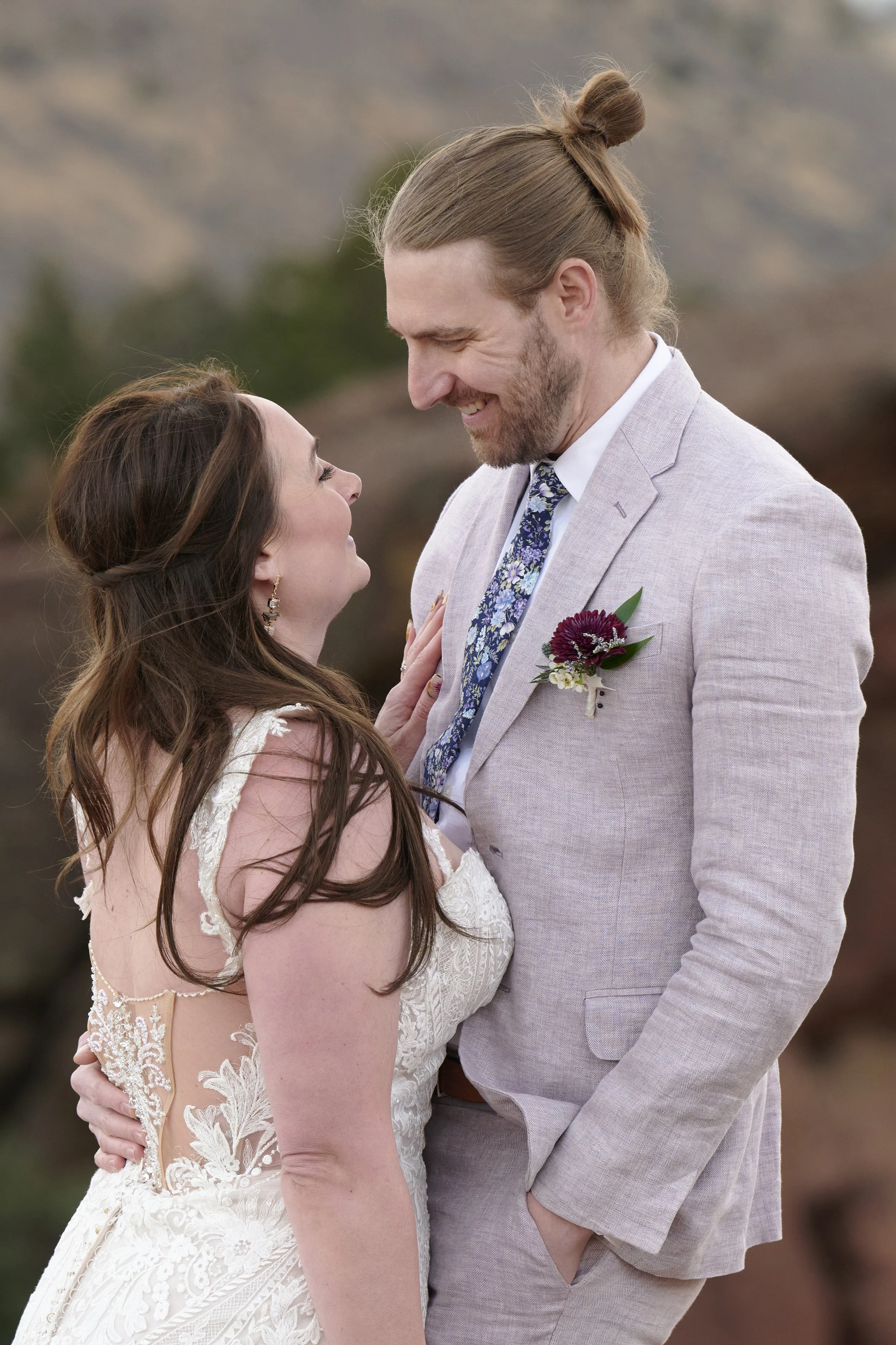 A bride and groom sharing a romantic moment outdoors, gazing into each other's eyes, with hills or mountains in the background.