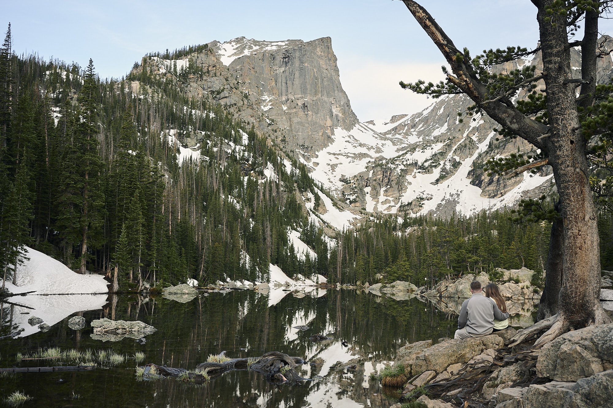 A couple sits on the lake shore of Dream Lake in Rocky Mountain National Park during an engagement photoshoot.