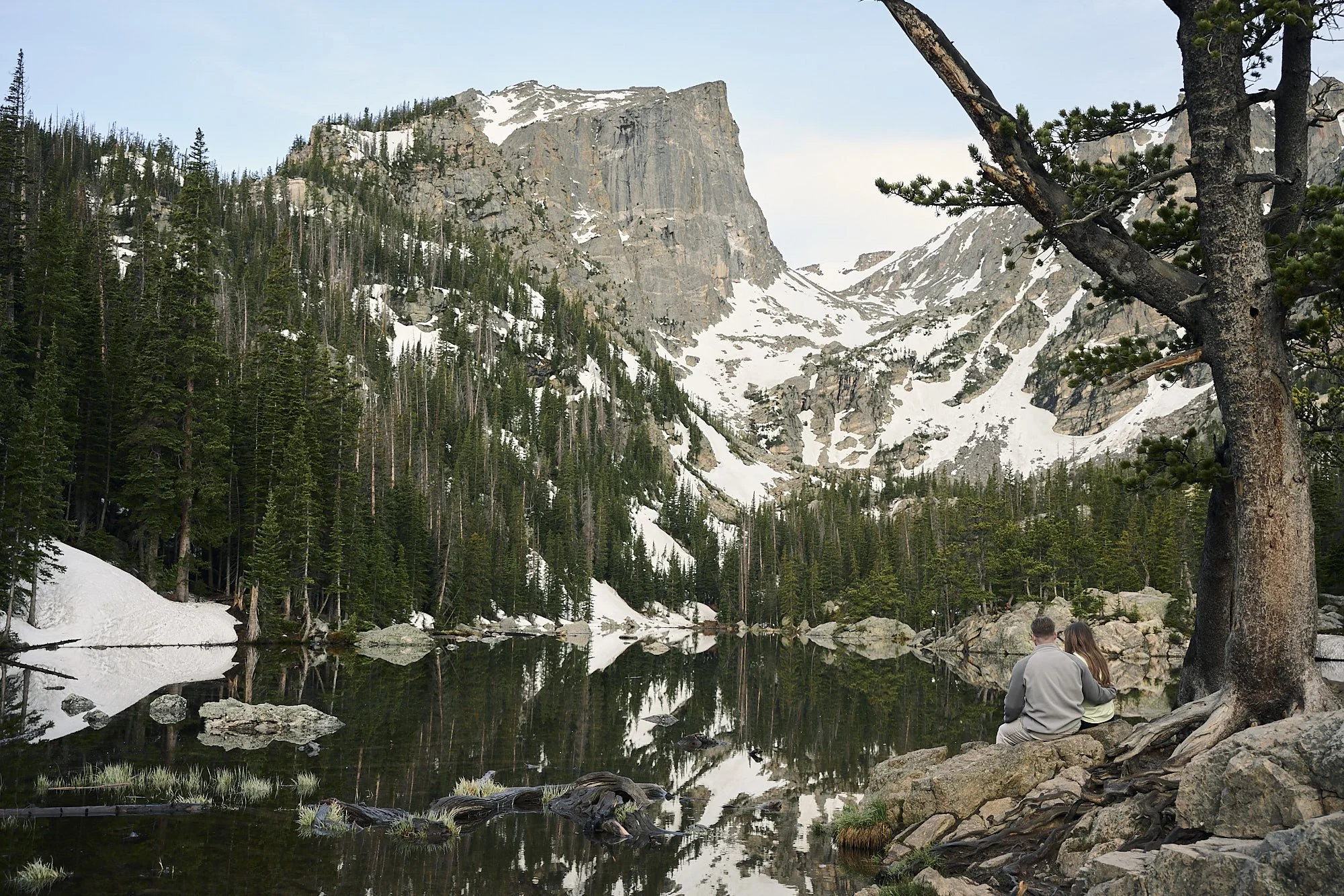 A couple sits together looking over the calm waters of Dream Lake with the iconic Mountain View in the background.