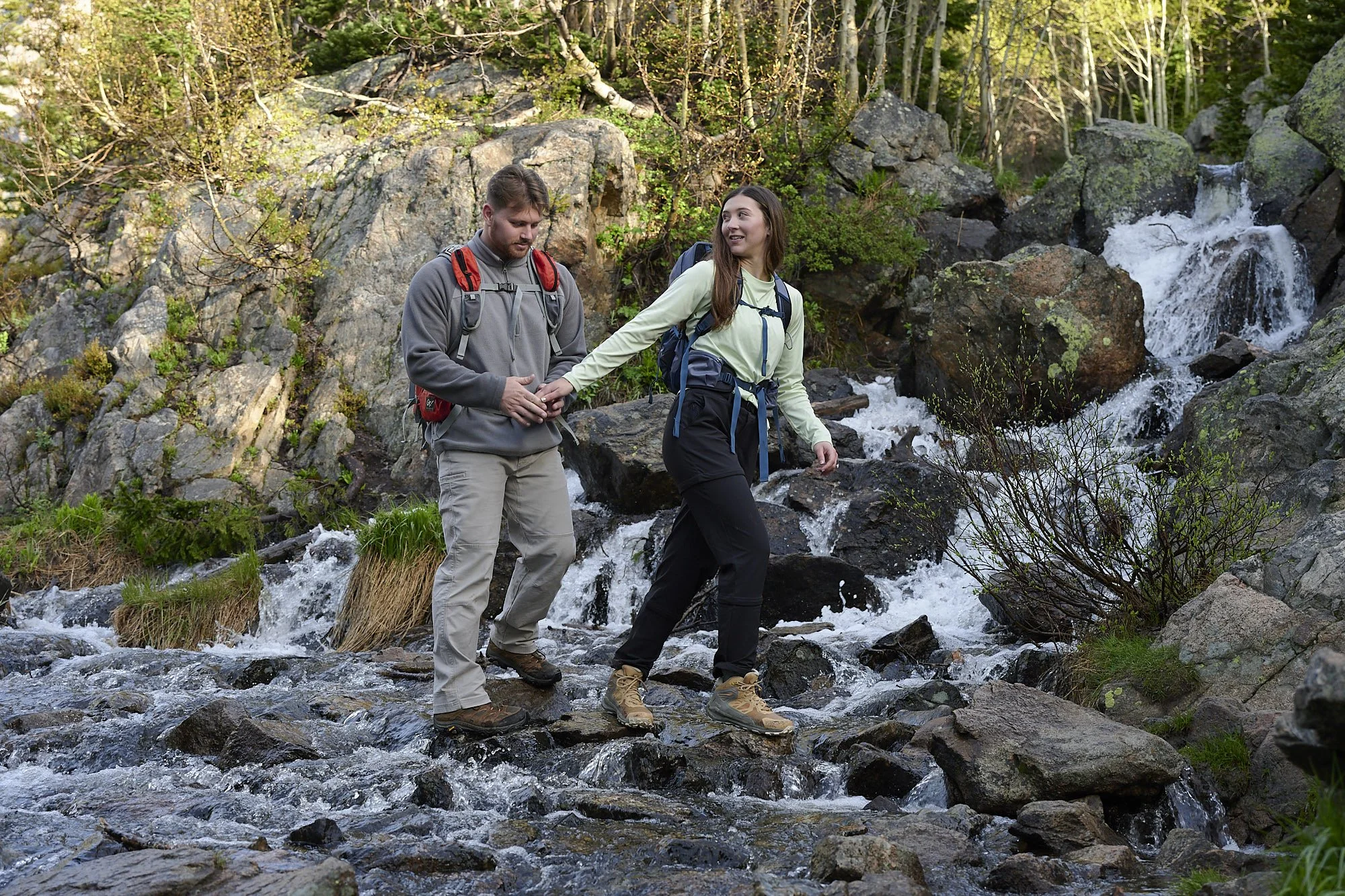 A couple holds hands while crossing a creek on the trail to Dream Lake.
