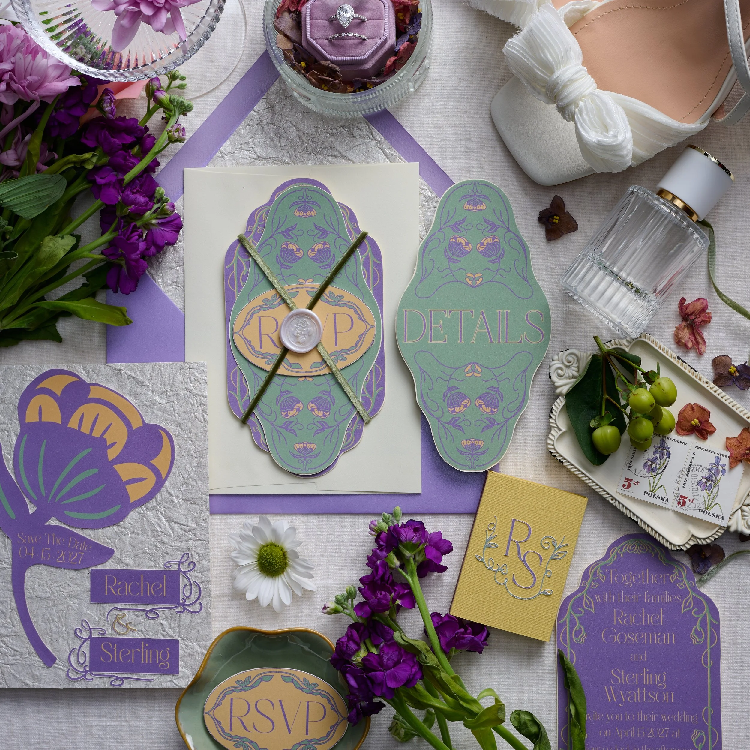 A flat lay of wedding stationery and accessories, including save-the-date cards, RSVP cards, detailed labels, and embellishments, accompanied by purple and white flowers, a perfume bottle, a ring in a purple box, and a white high-heeled shoe.