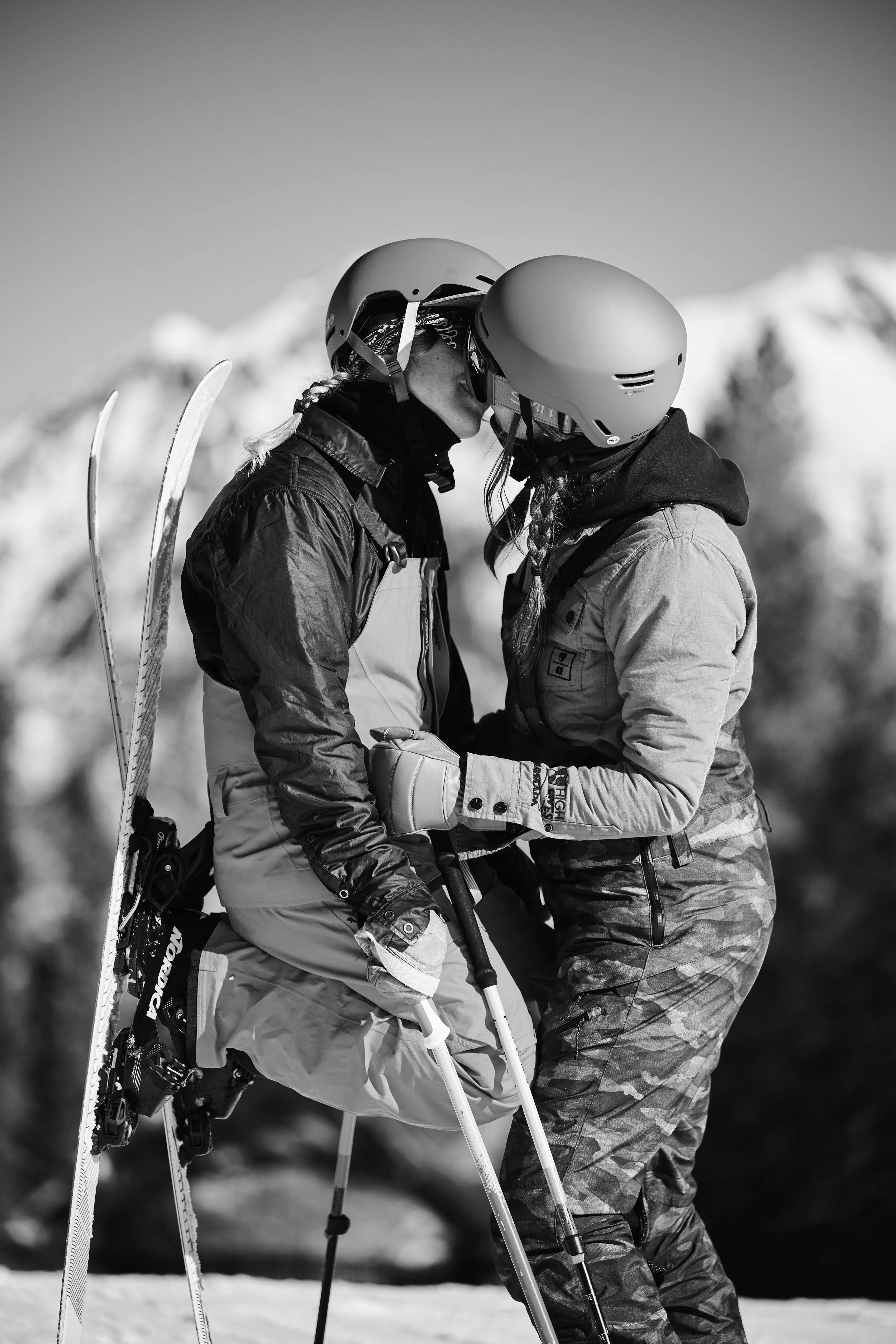 Two women in ski gear kissing in a snowy mountain setting.