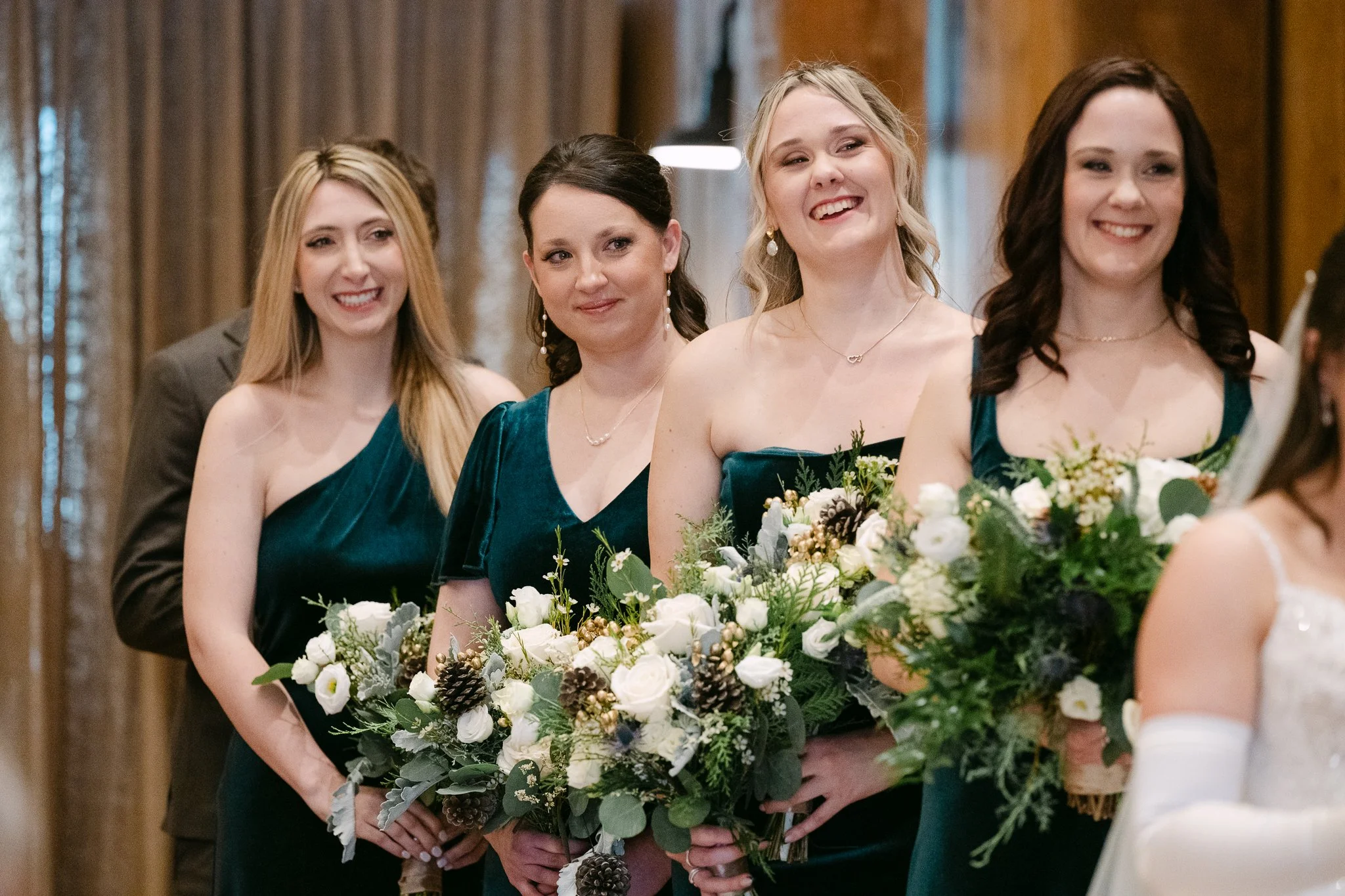 Four women in teal dresses holding bouquets at a formal event or wedding