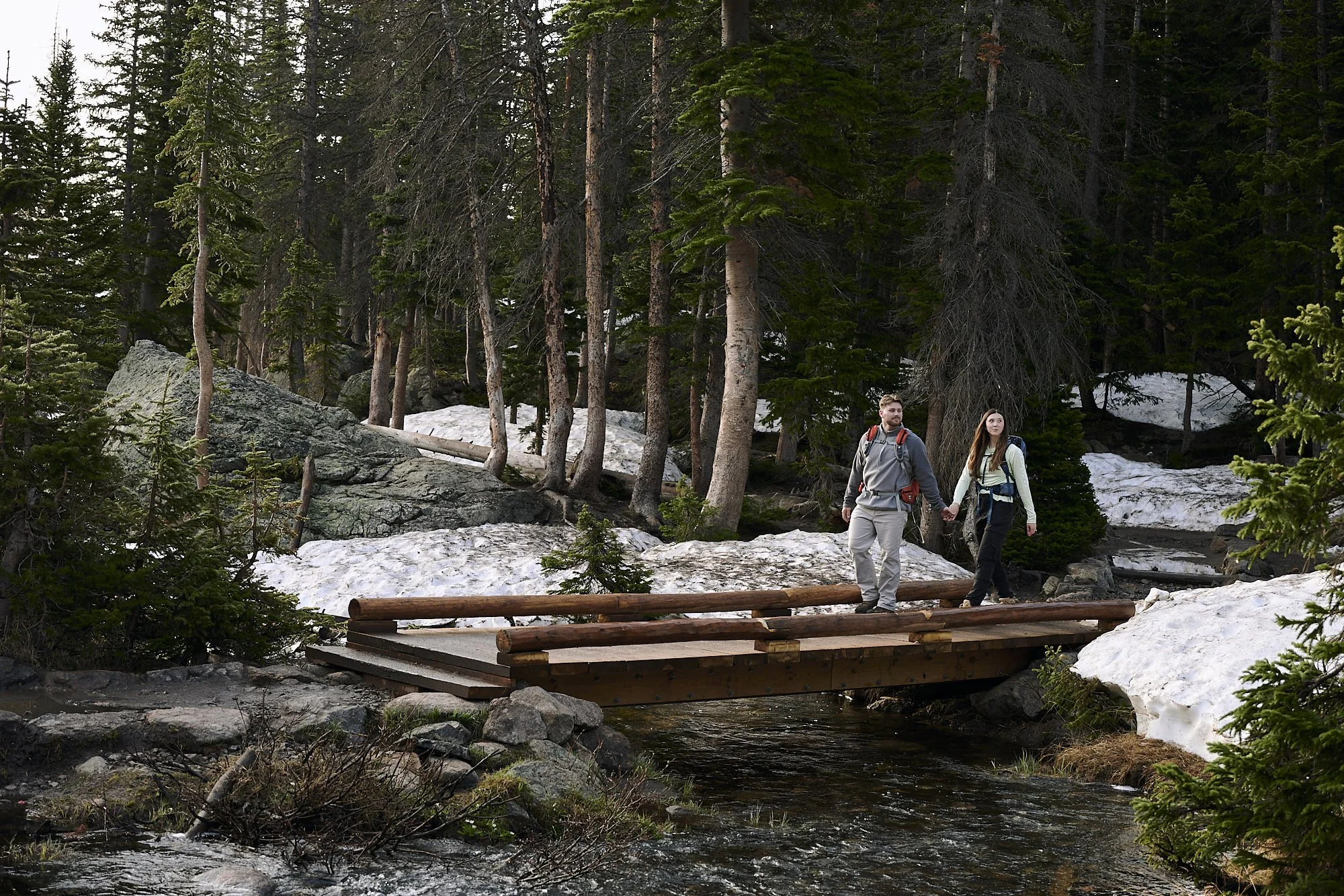A couple hold hands as they cross a footbridge leading to emerald lake and dream lake.