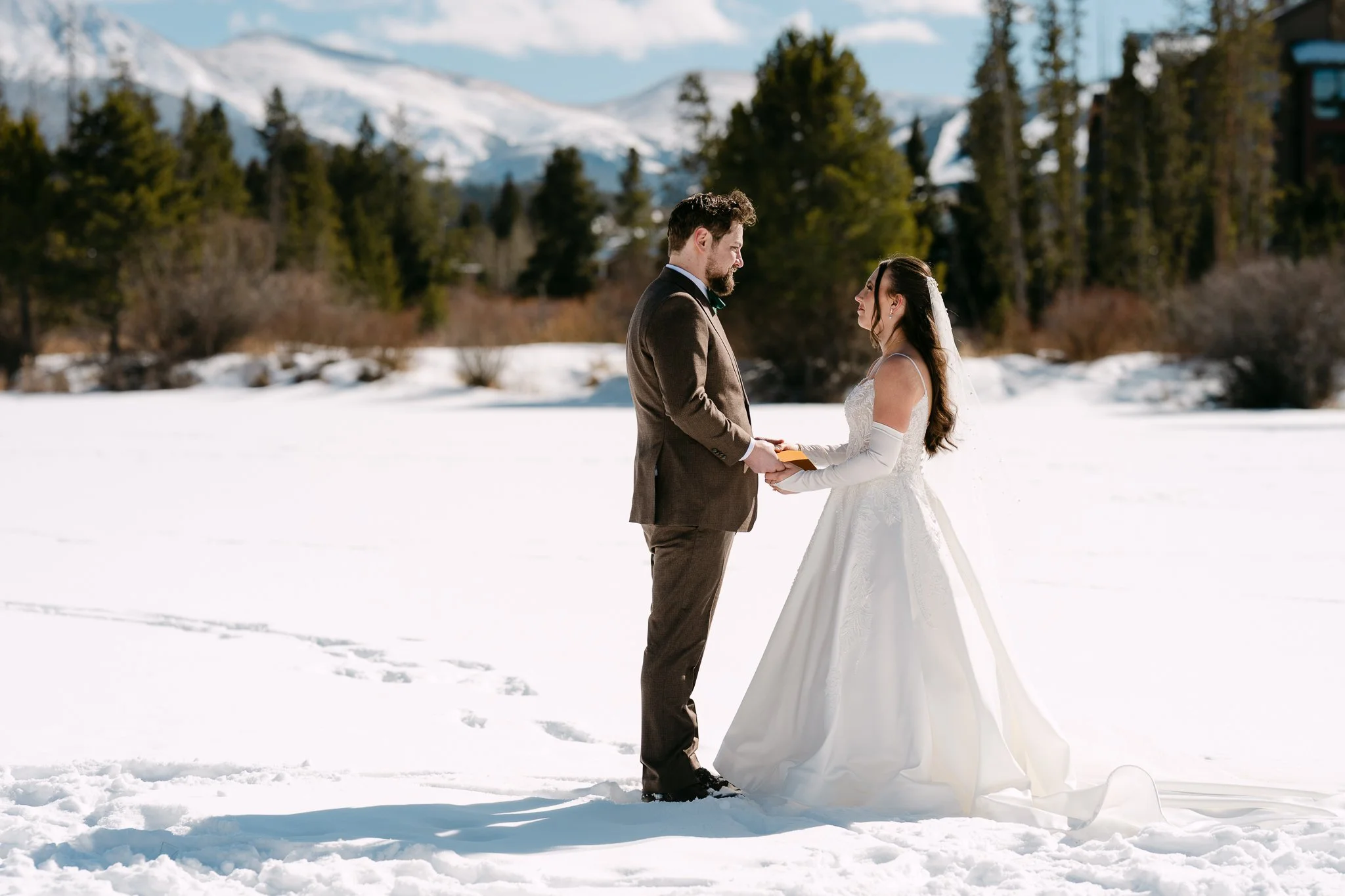 A couple holds hands in their wedding attire on a lake outside their wedding venue in winter park Colorado