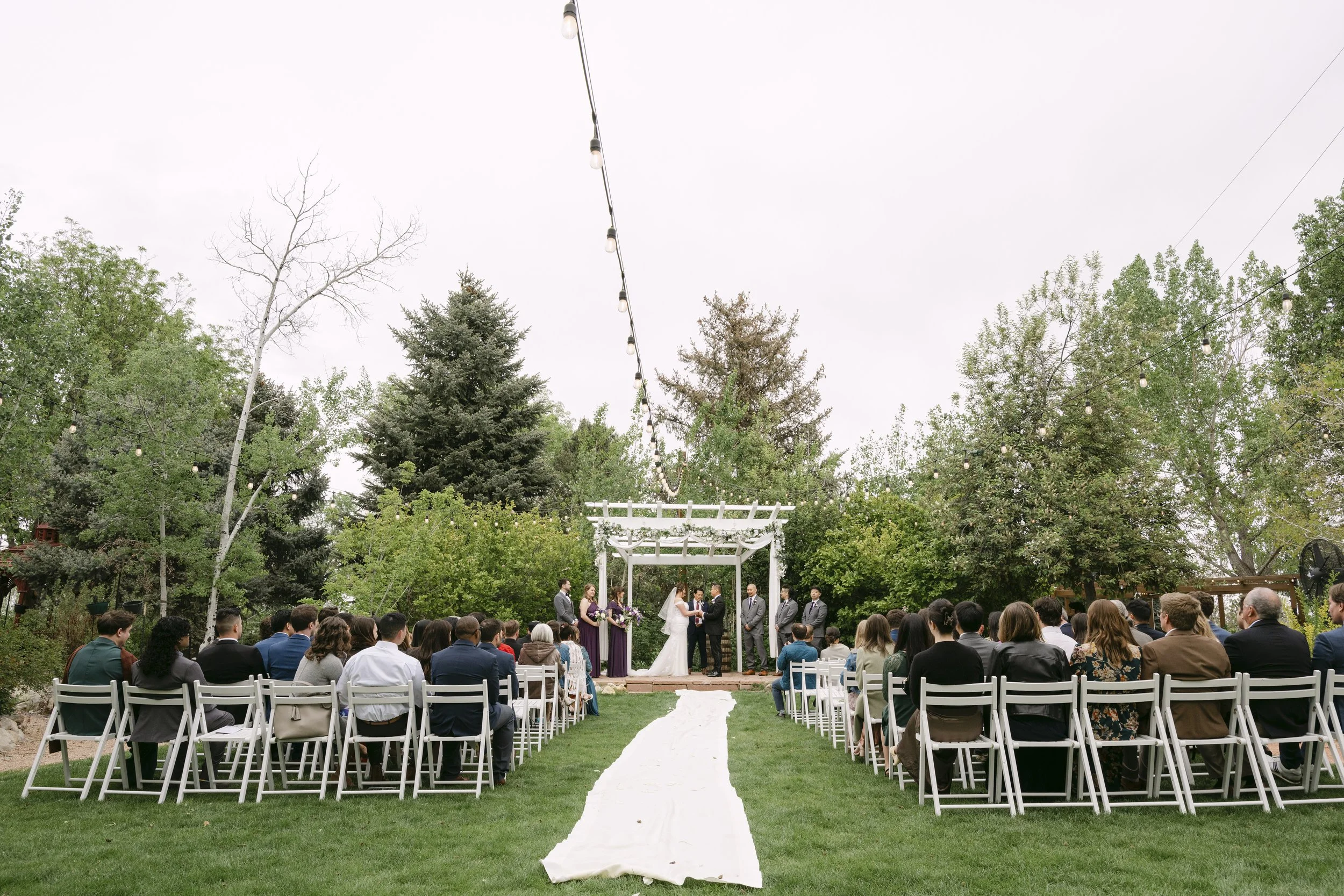 A wedding happening a the Church Ranch Event Center grounds in early spring bloom, with the stone ceremony stage and surrounding aspens.