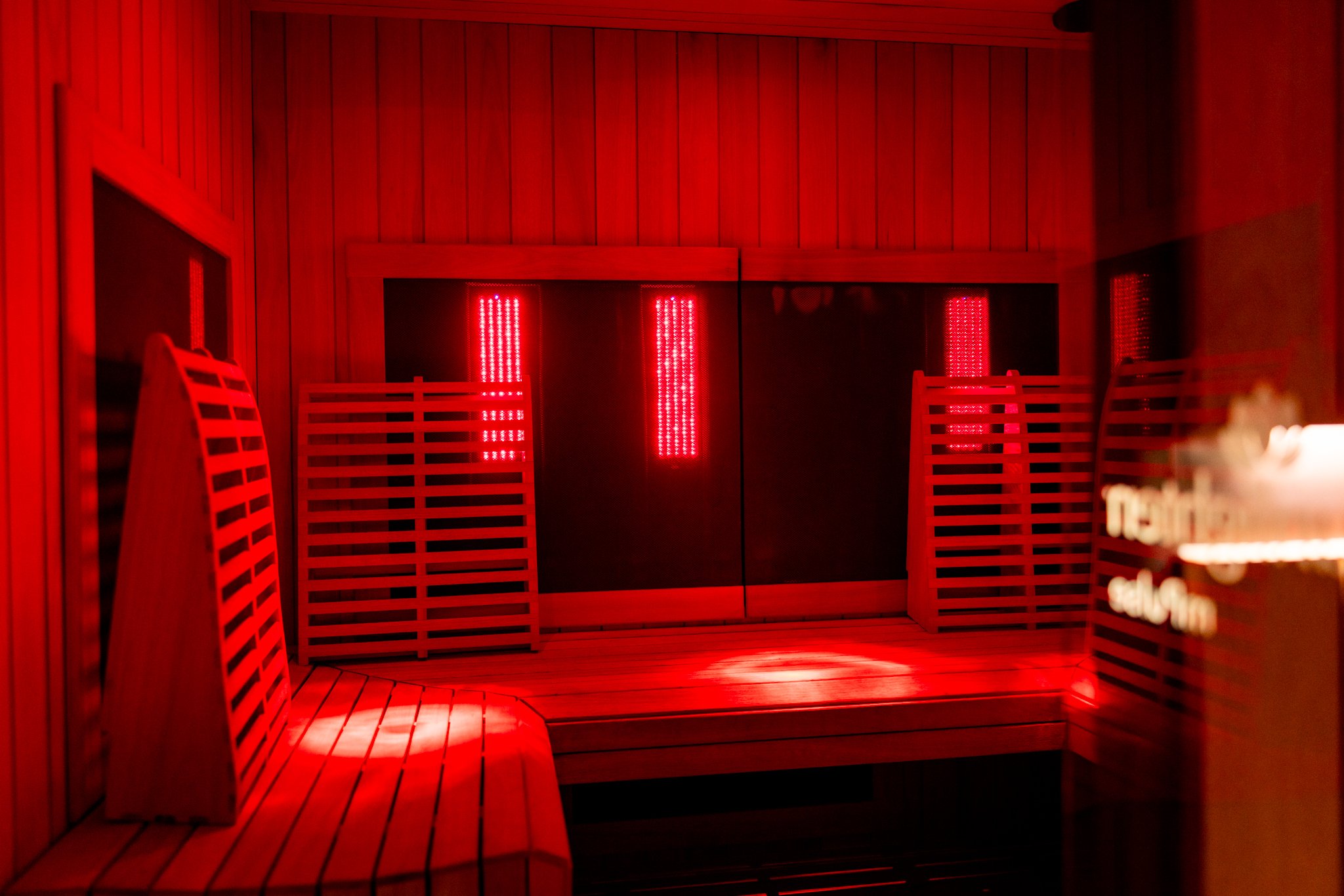 An infrared sauna room with wooden walls, benches, and red lights.