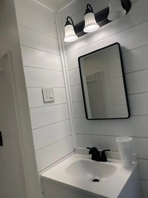 Bathroom sink with black faucet, mirror on white shiplap wall, and two white sconces above.