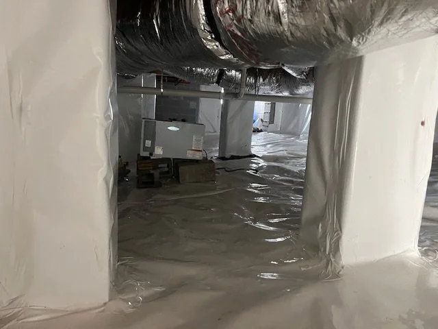 Construction site with ducts and wrapped support columns, with plastic sheeting on the floor.