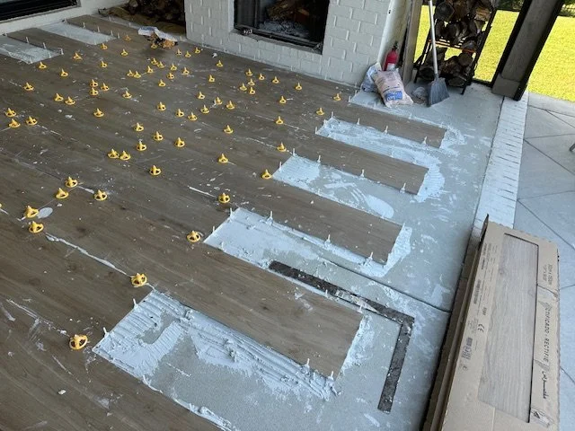 Installing new hardwood flooring with underlayment and spacers in a living room area near a fireplace.