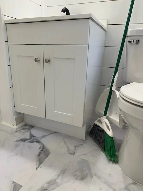 Bathroom with white cabinet, toilet, and green broom next to the toilet.