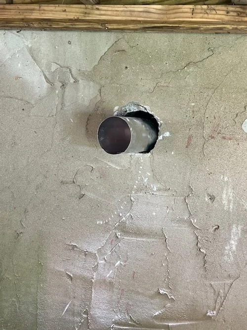 A concrete wall with a metal pipe protruding through a hole.