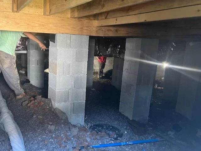 Construction workers building a foundation on concrete block supports under a wooden structure.