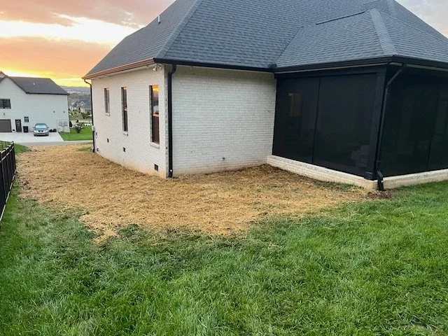 Side view of a house with a screened-in porch, grass, and a sunset sky in the background.