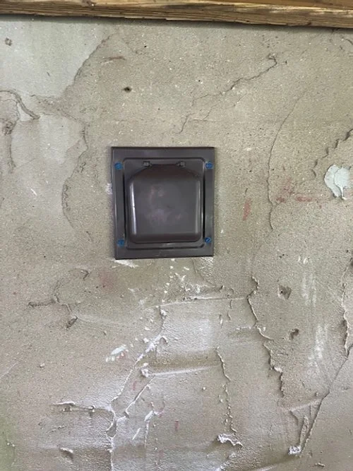 Close-up of a black electrical outlet or switch installed in a rough, unfinished concrete wall.