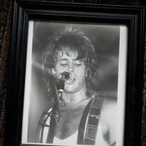 Black and white photograph of a woman singing into a microphone with curly hair, framed and mounted on a wall.