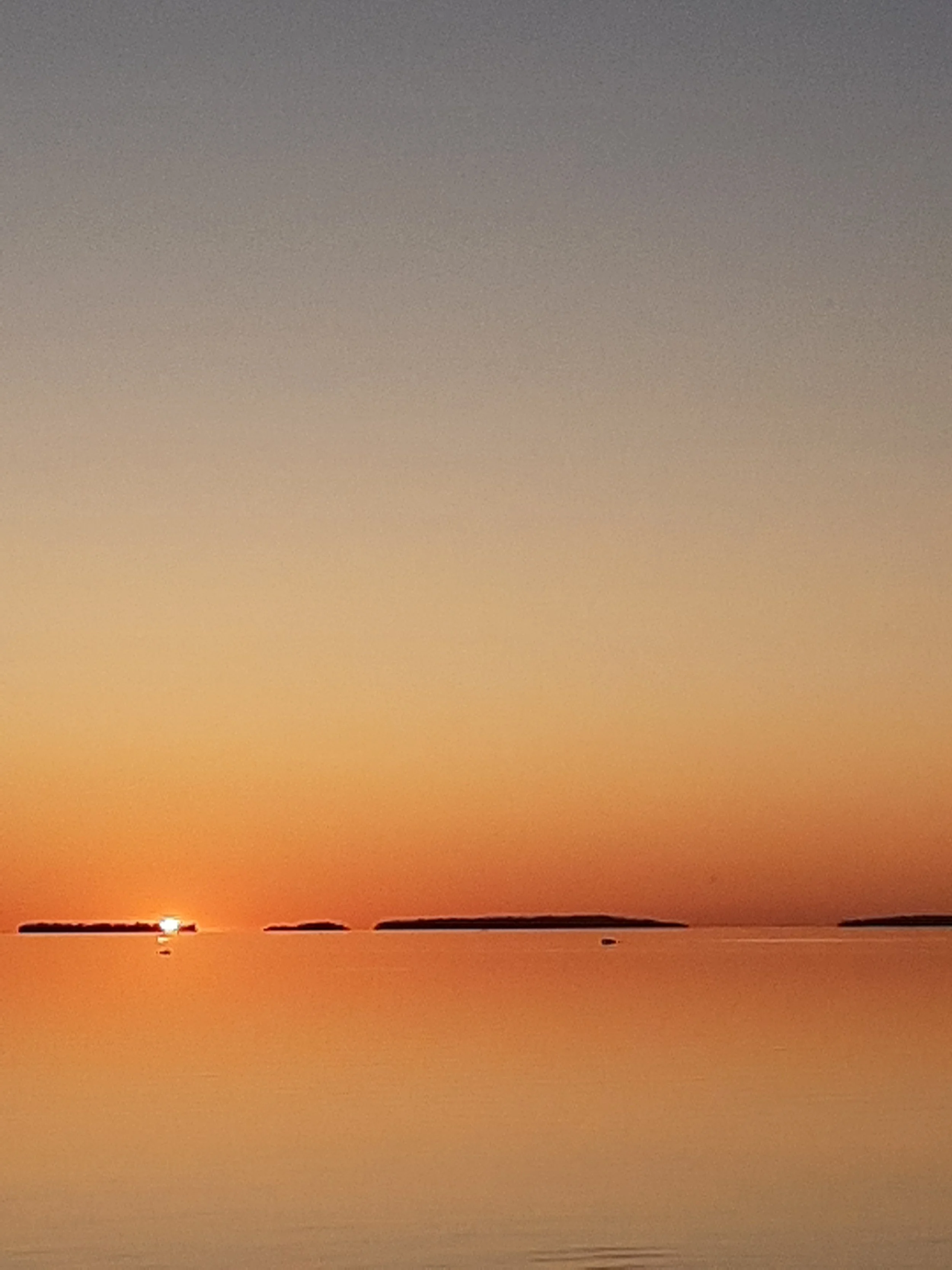 Calm water reflecting a sunset with distant islands and colorful sky.